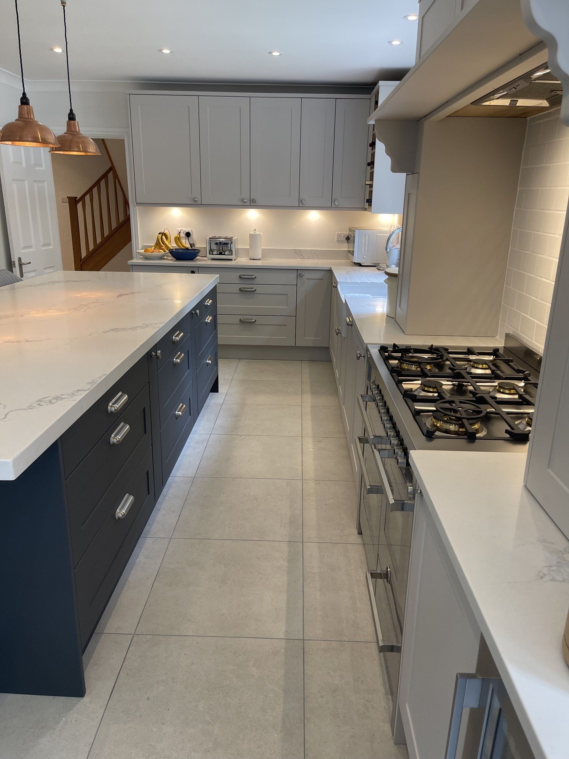 A modern kitchen featuring a dark blue island with a white countertop and light grey perimeter cabinets with a gas range.
