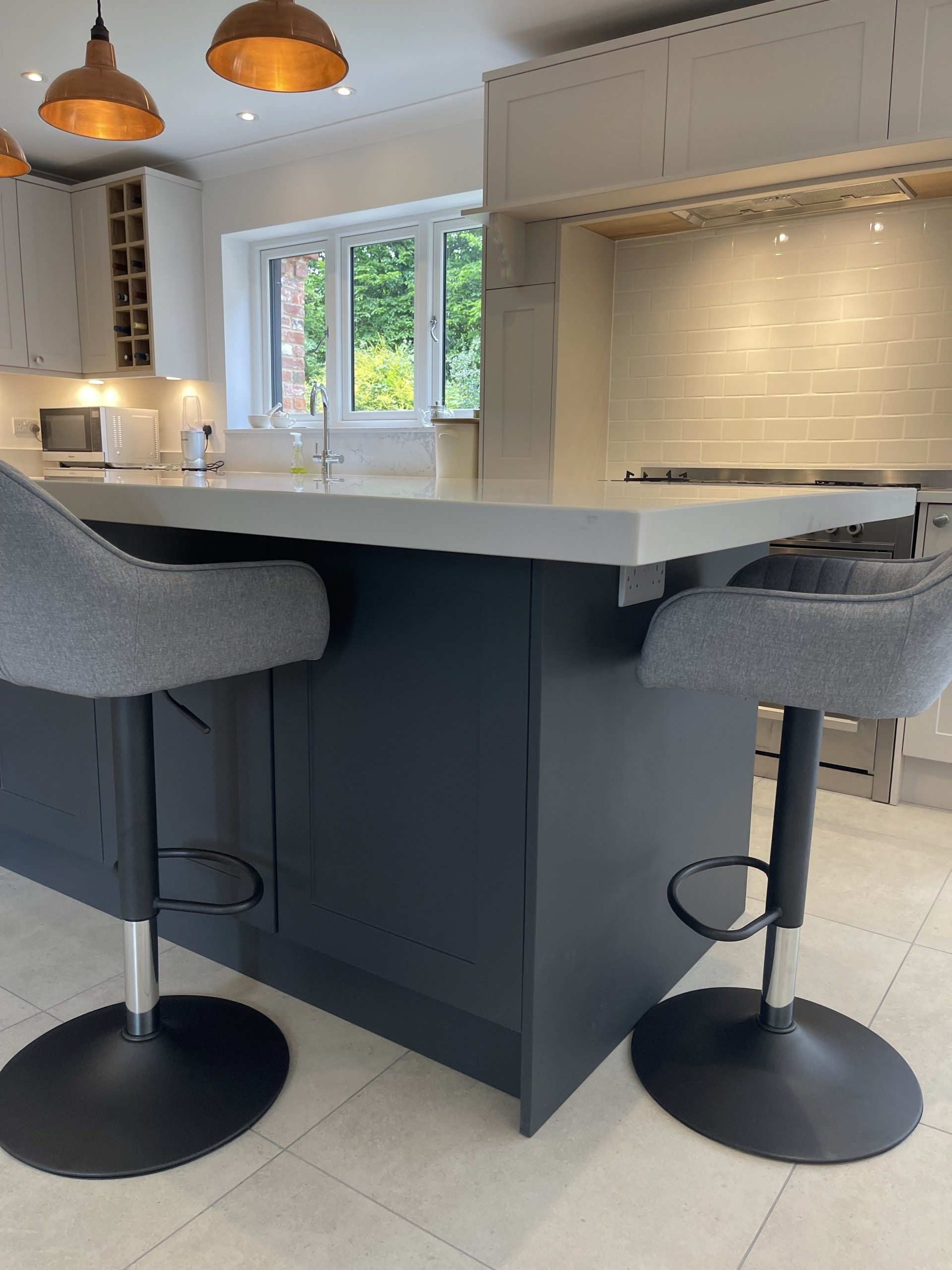 A kitchen island with a white countertop and dark base, featuring two grey bar stools, in a modern, well-lit kitchen.