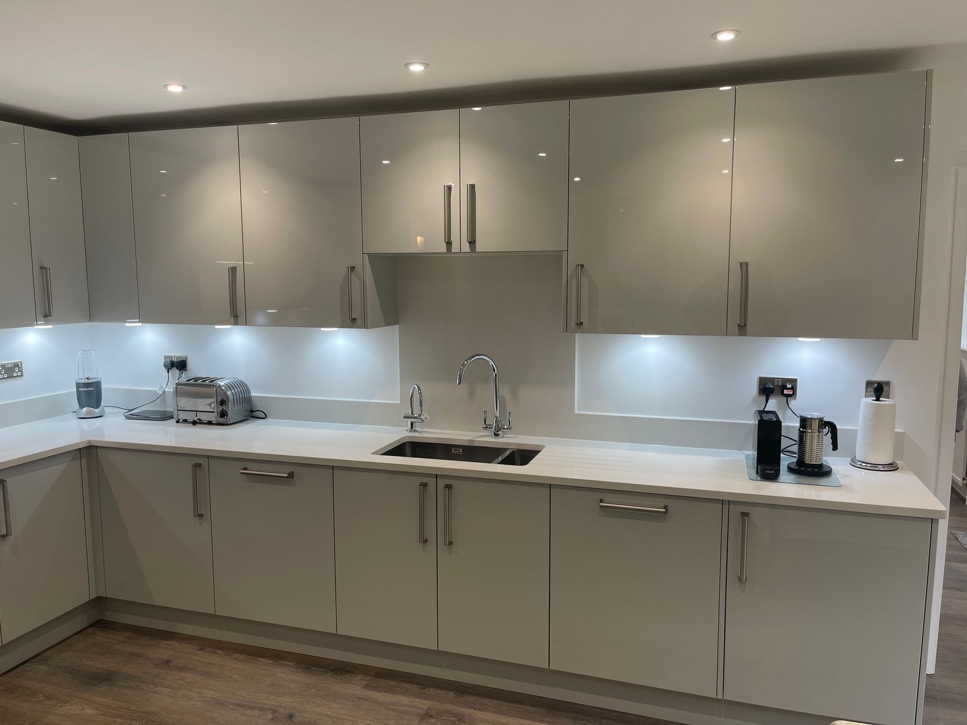Modern kitchen featuring glossy light grey cabinets, white countertops, a stainless steel sink, and recessed lighting.