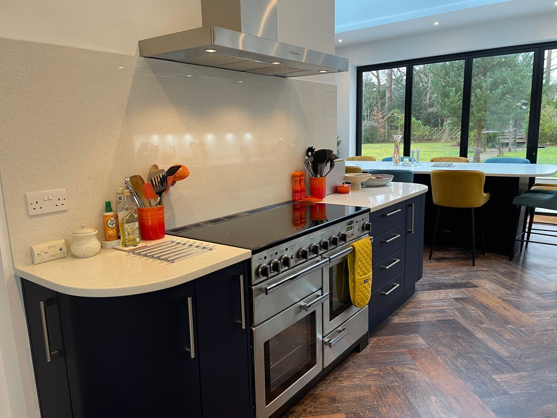 A navy blue kitchen with white countertops, a large stainless steel range cooker, and a dining area with yellow chairs.