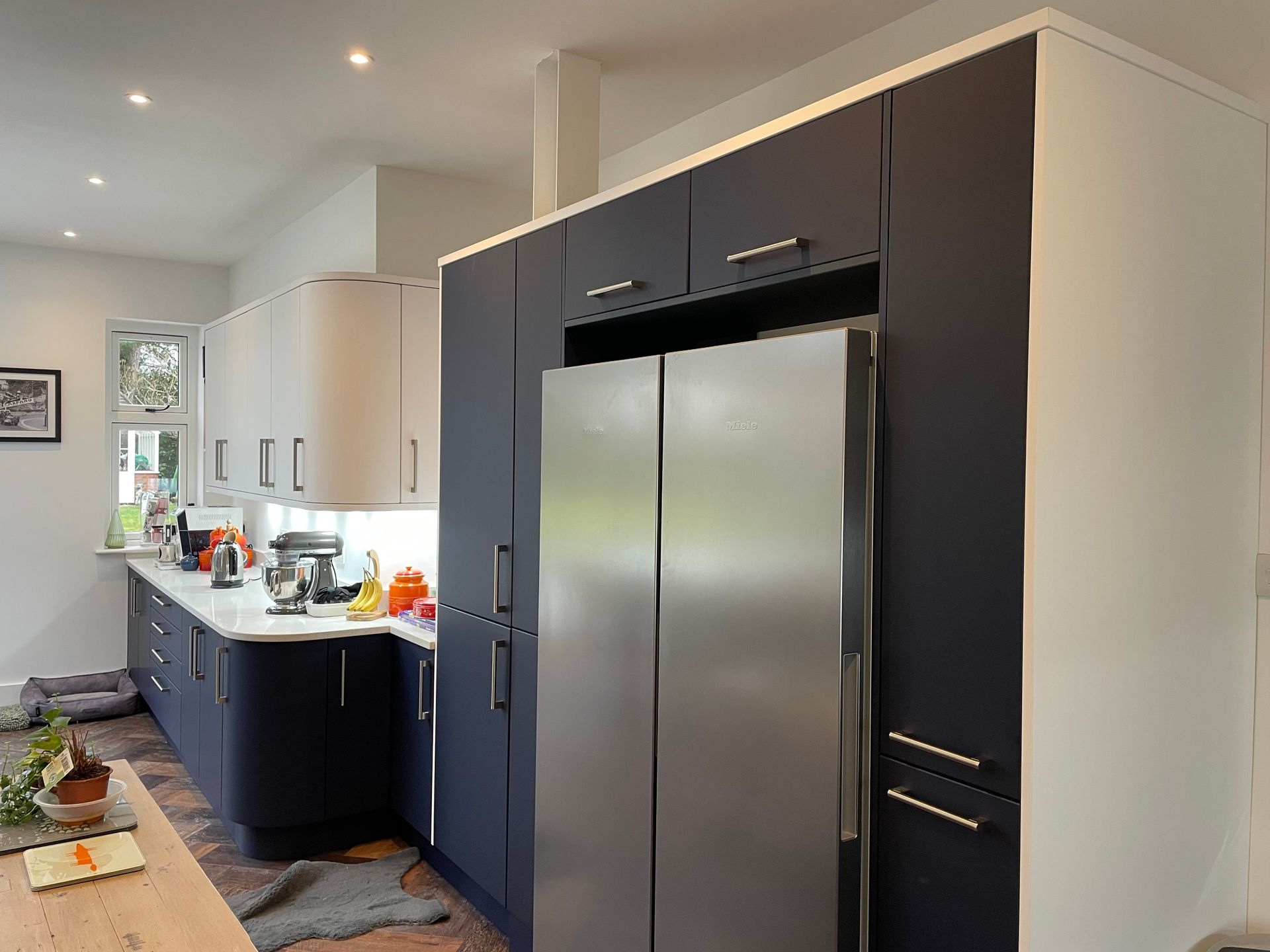 A modern kitchen with dark blue cabinetry, a stainless steel side-by-side refrigerator, and white countertops.