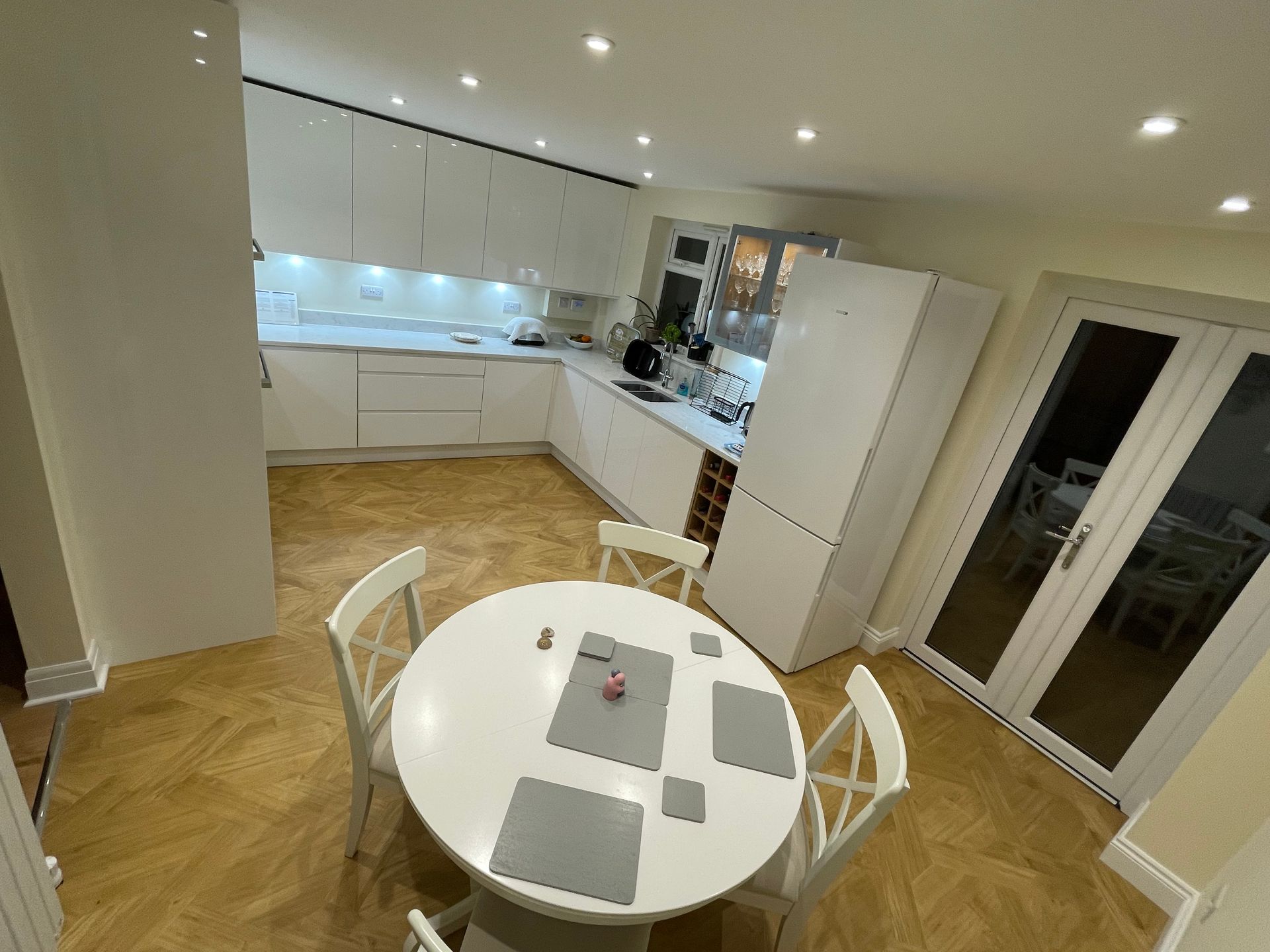 A modern kitchen with white cabinetry, a round table with four white chairs, and light wood flooring.