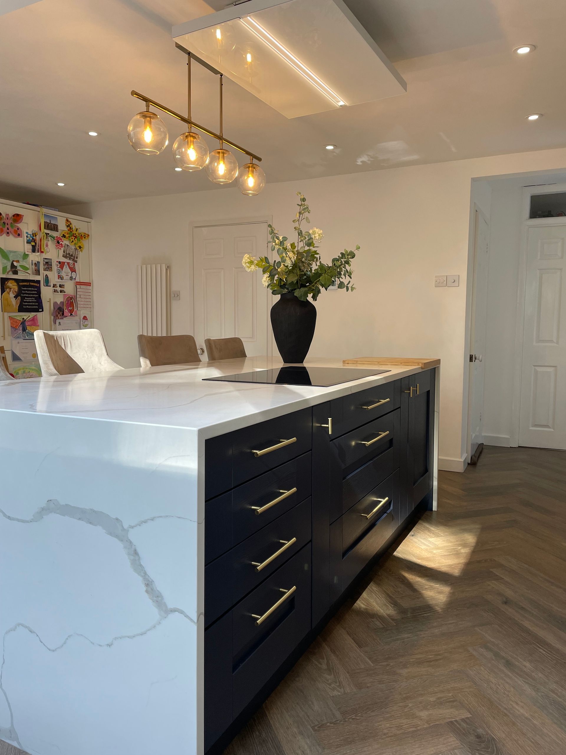 A dark blue kitchen island with a white marble-patterned countertop, topped with a black vase and floral arrangement.