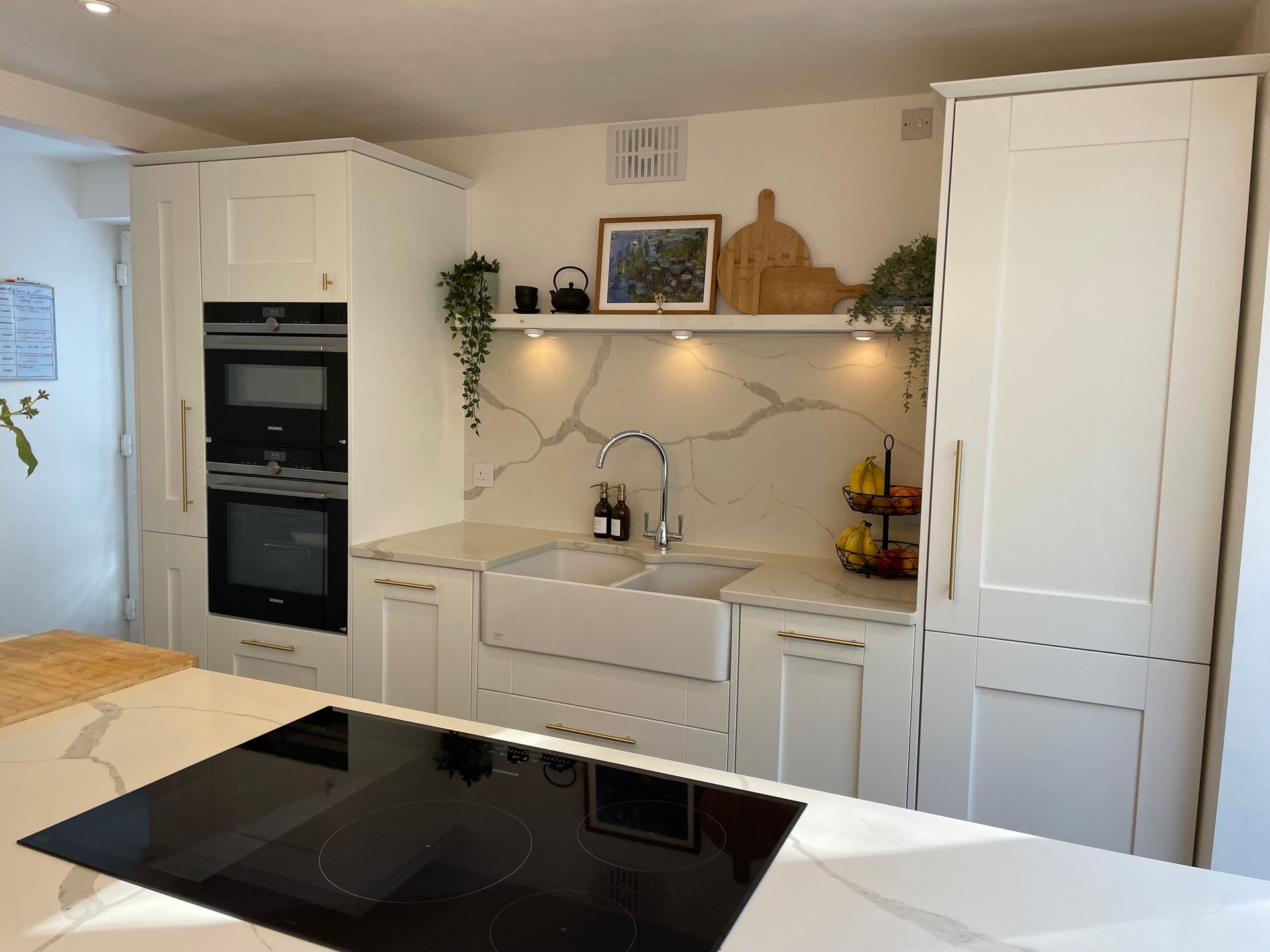 A bright, modern kitchen featuring white shaker cabinets, a farmhouse sink, marble-veined backsplash, and a black cooktop.