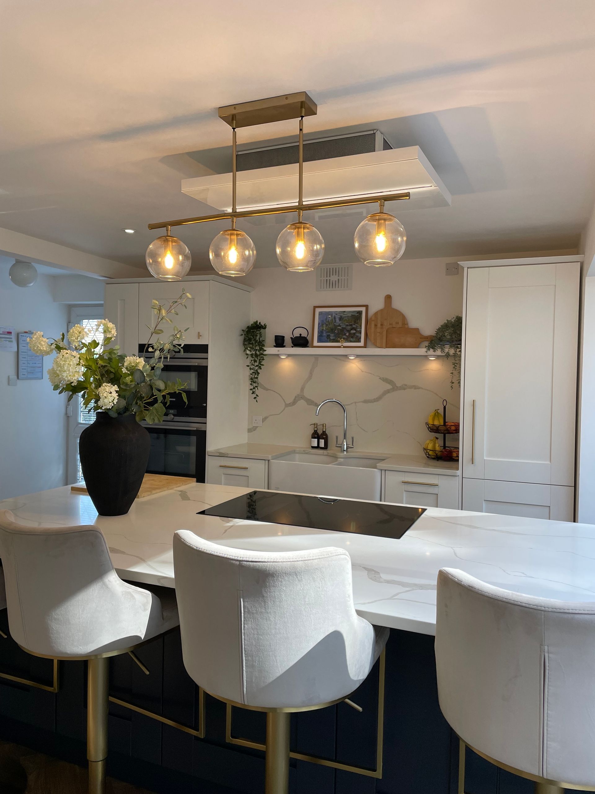 A modern white and dark blue kitchen featuring a marble-topped island, four glass globe pendant lights, and bar stools.