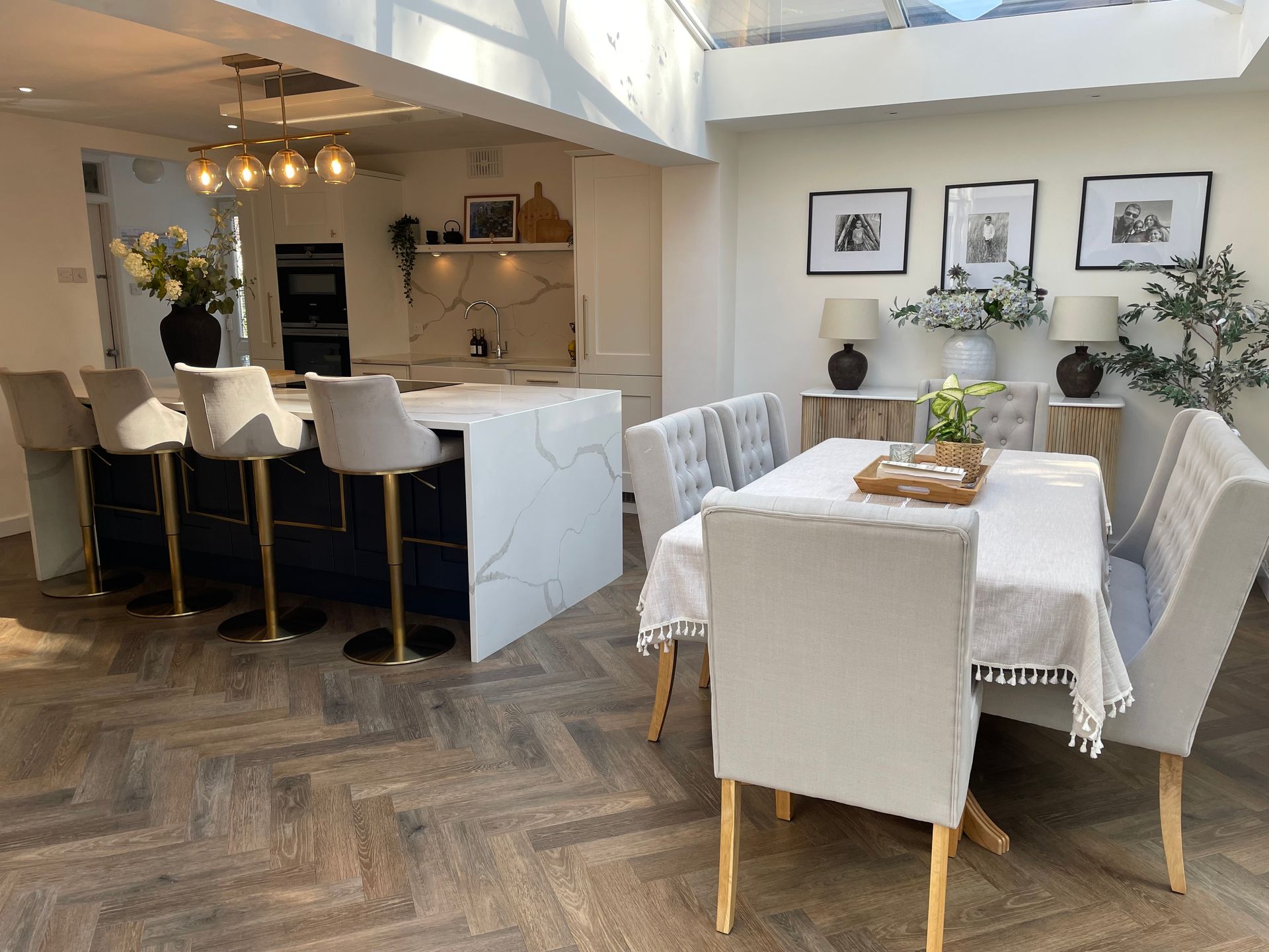 Modern open-plan kitchen and dining area with a marble-topped island, light-colored upholstered chairs, and wood flooring.