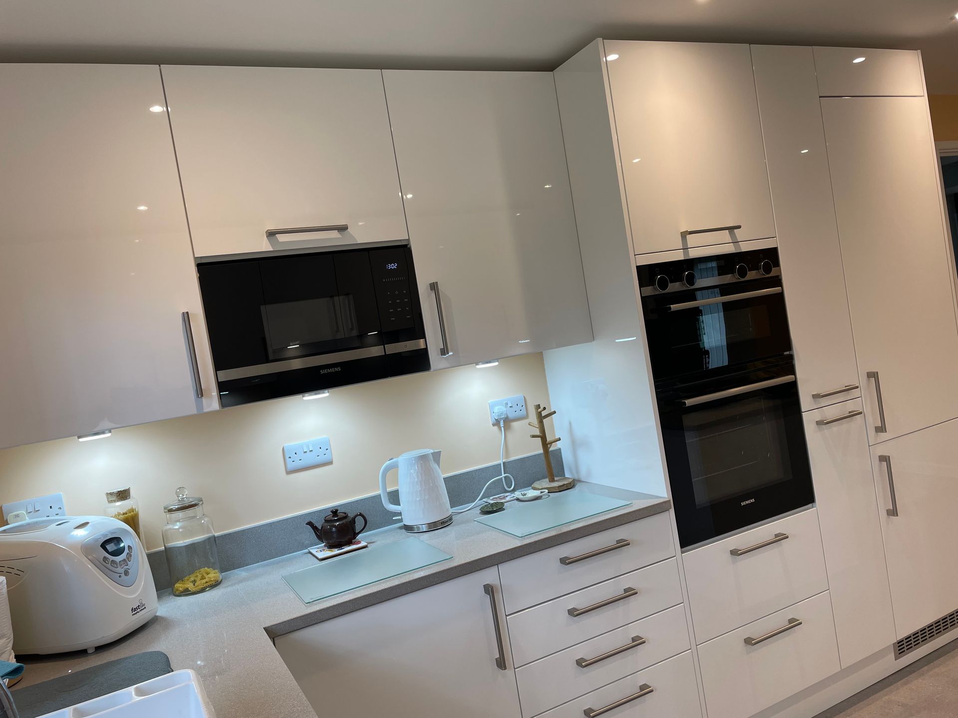 A modern kitchen featuring glossy cream-colored cabinetry, a built-in oven, a microwave, and white countertops.