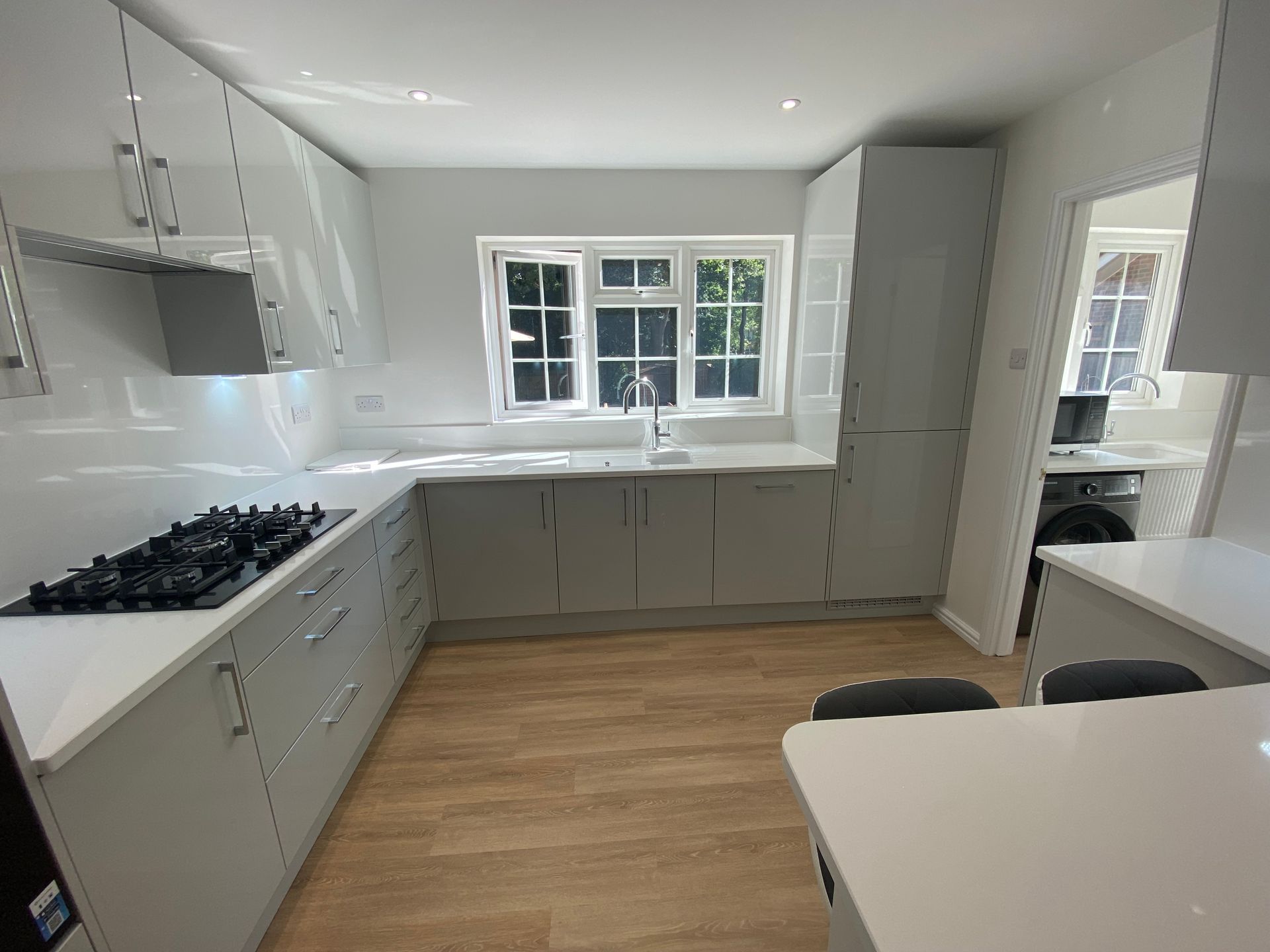 A modern, L-shaped kitchen with light gray cabinets, white countertops, a gas stove, and wood-look flooring.