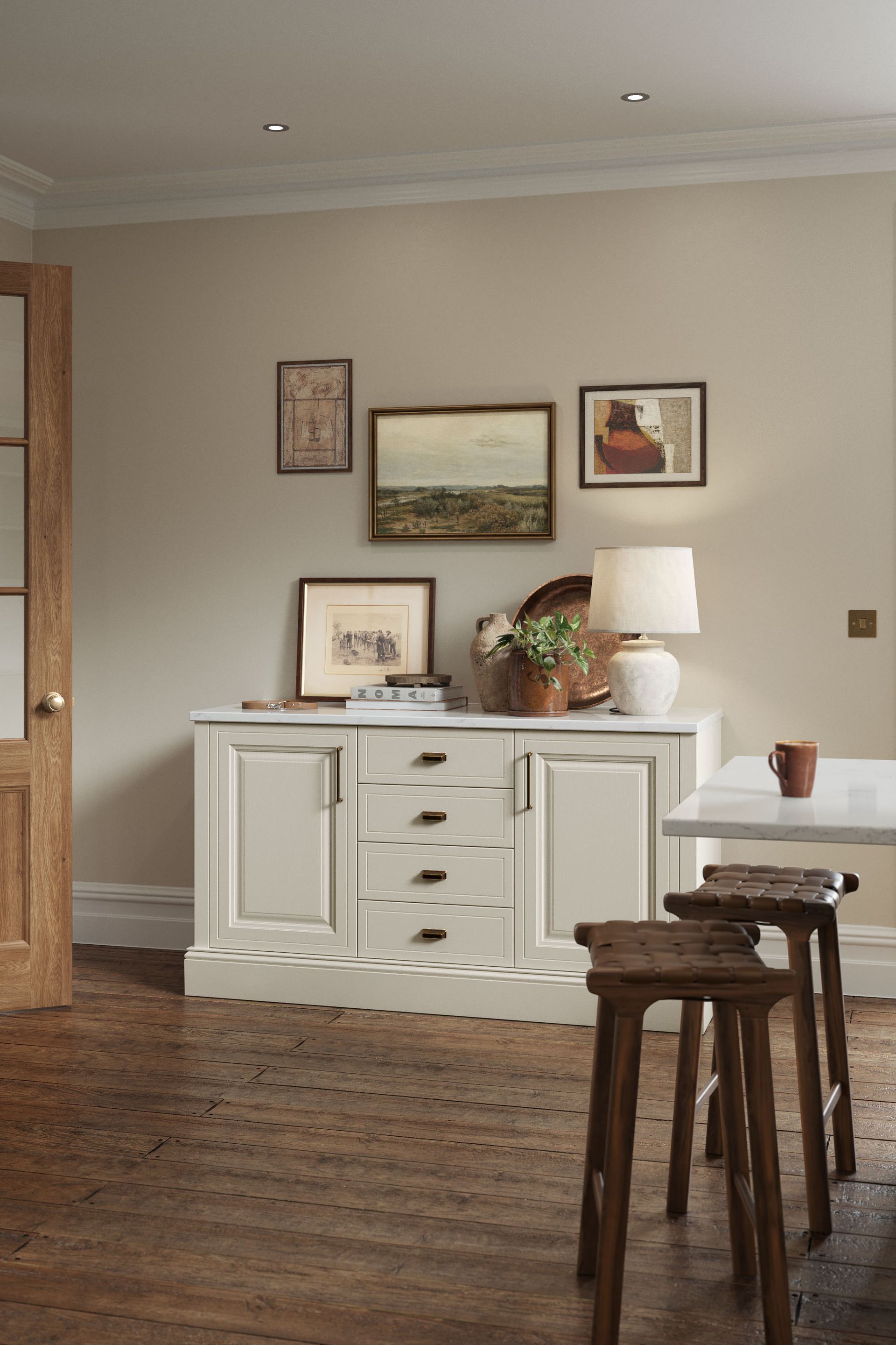 A white sideboard sits against a beige wall, topped with a lamp and framed art. Two wooden stools stand in the foreground.