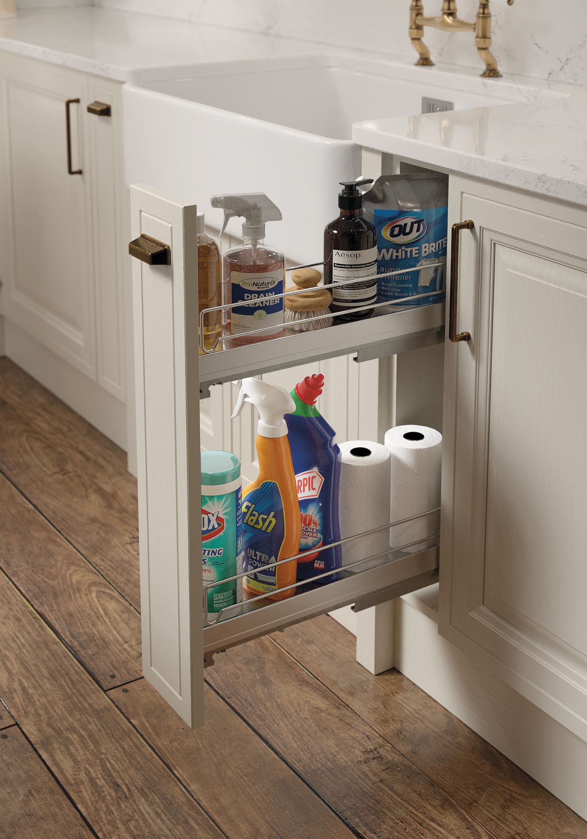 A pull-out kitchen cabinet organizer filled with cleaning supplies and paper towels next to a farmhouse sink.