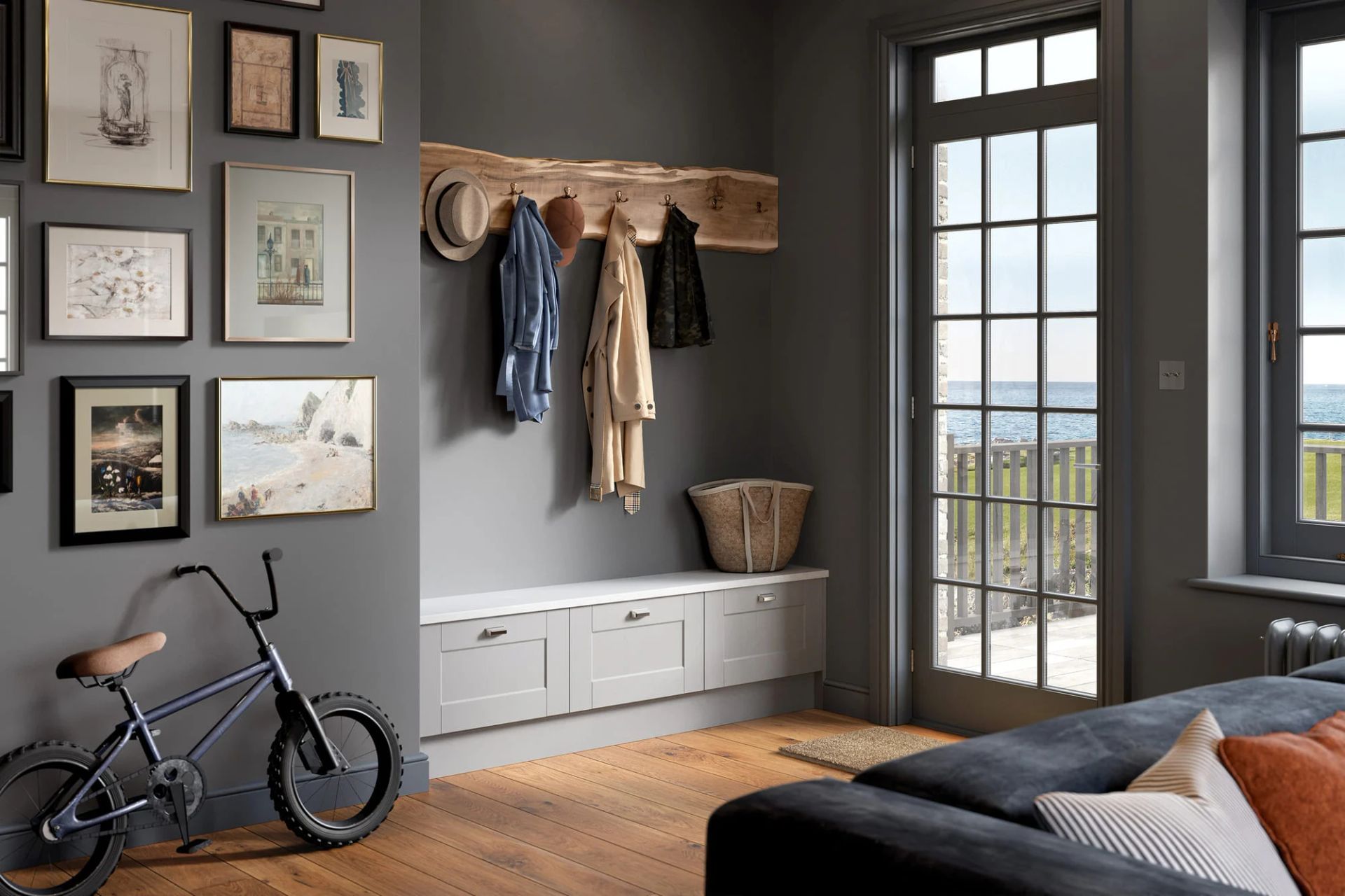 An entryway with a gray wall, a wooden coat rack, light gray storage bench, framed artwork, and a small bicycle.