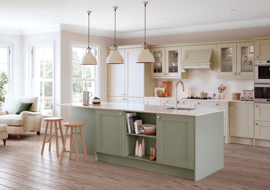 A sage green kitchen island stands in a bright, modern kitchen with cream-colored cabinetry and wooden floors.
