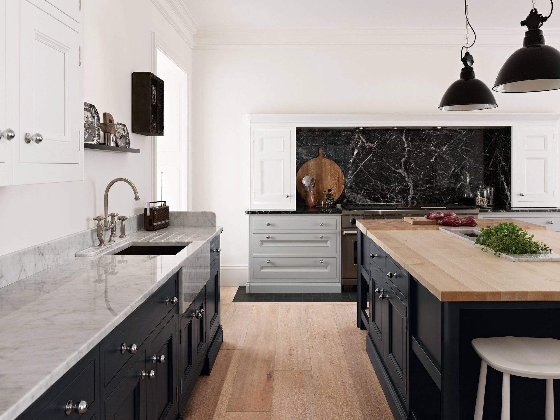 A modern kitchen with dark blue cabinets, marble countertops, light wood floors, and a black marble backsplash.