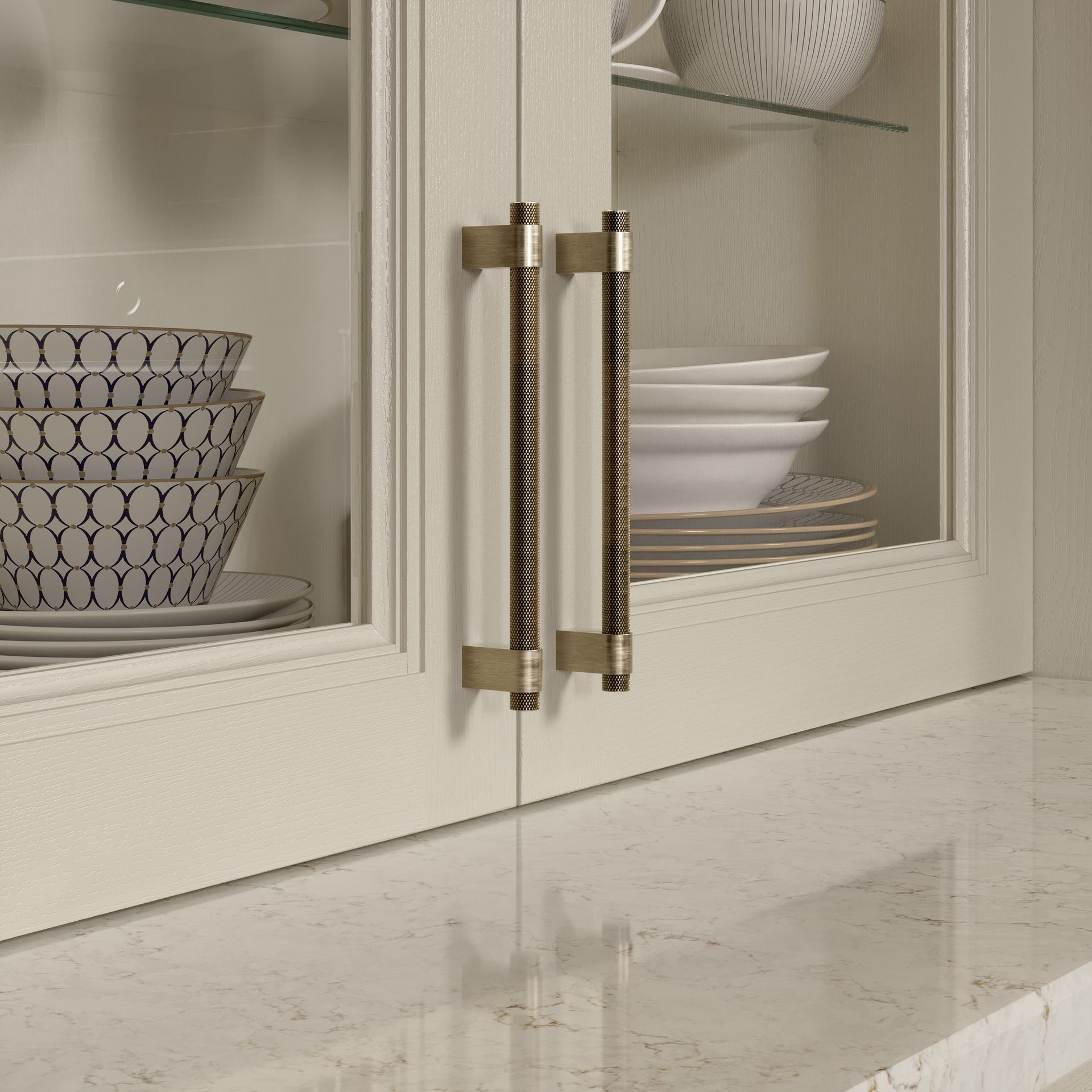 White kitchen cabinet with glass doors, brass handles, and stacked dishes inside.