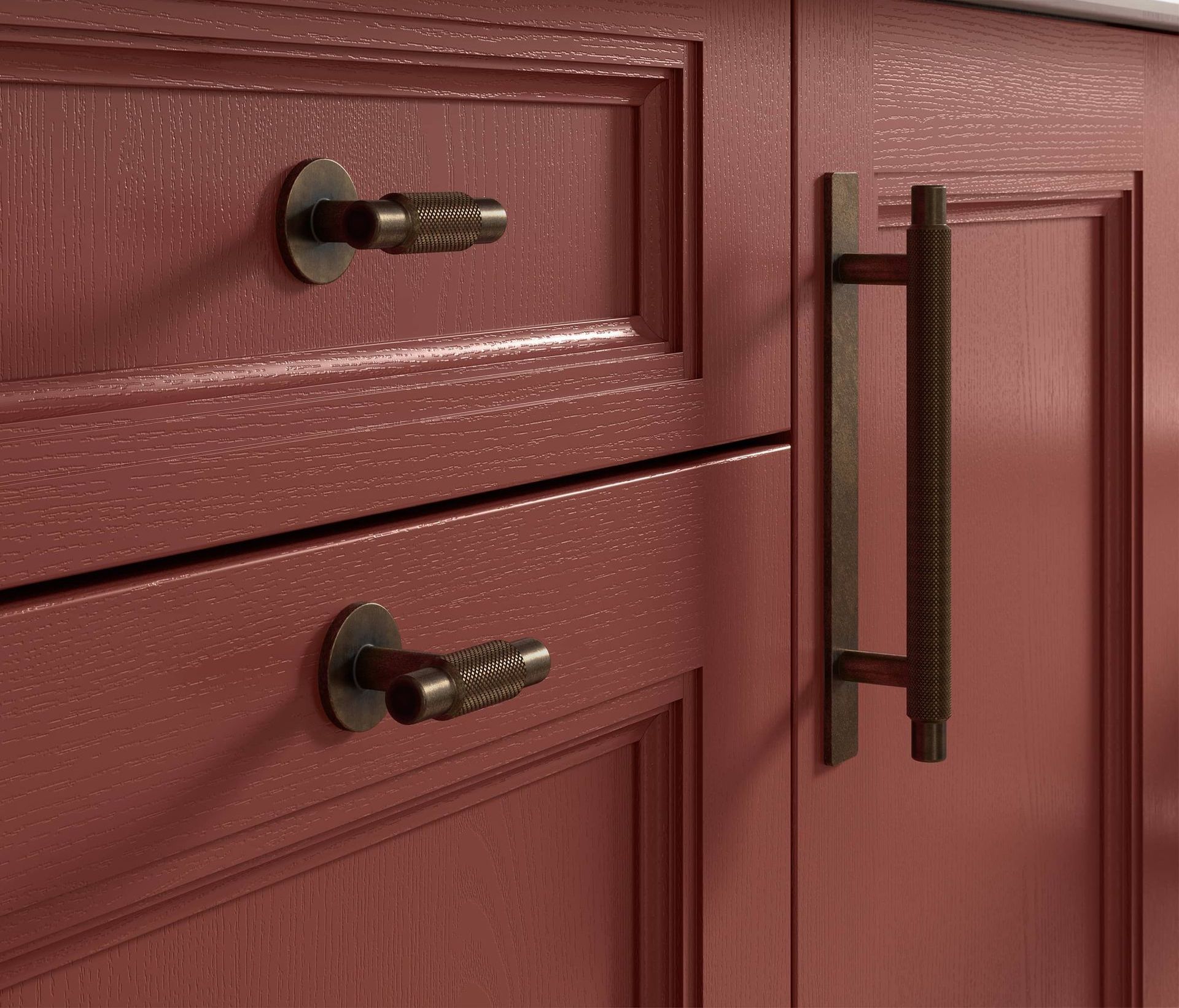 Close-up of burgundy cabinet drawers and door with black pulls and a long vertical handle