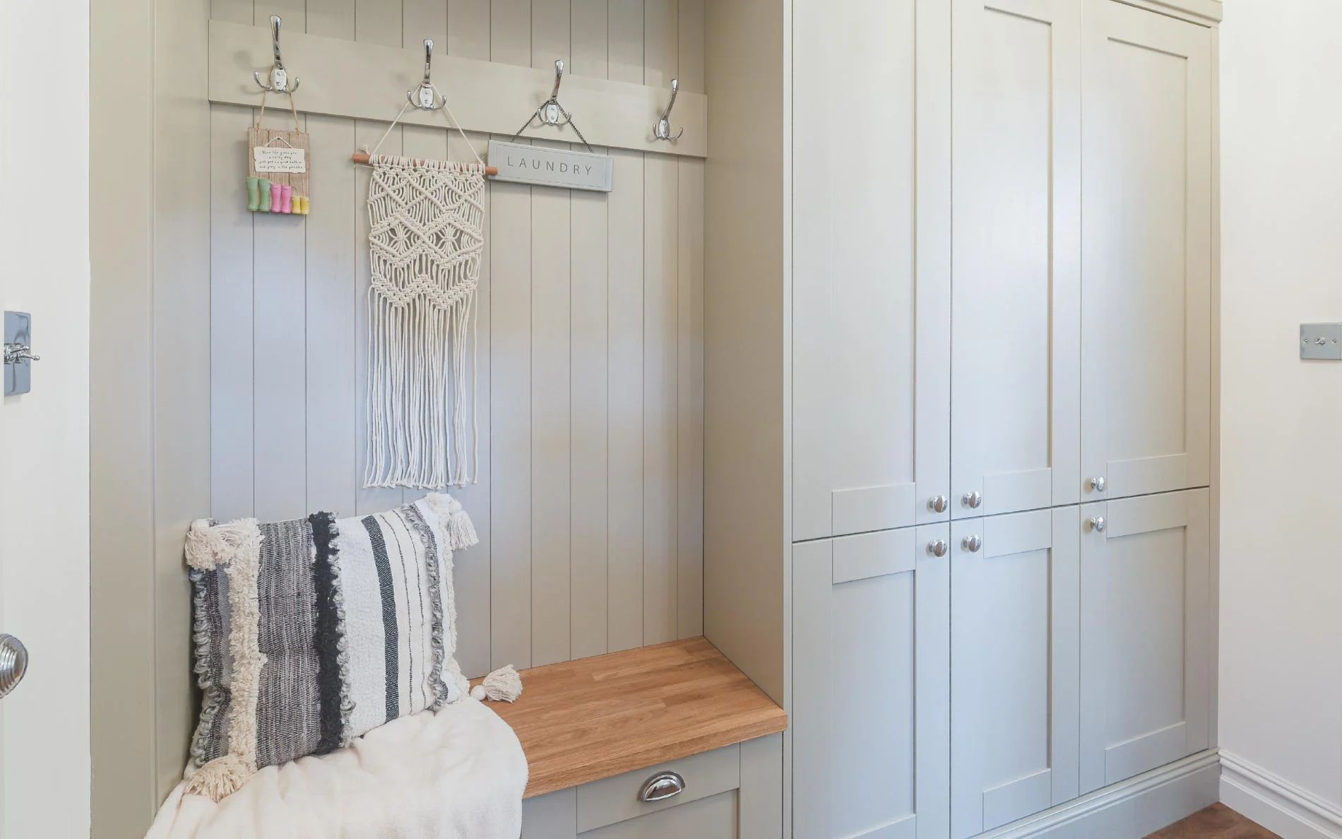 A built-in mudroom bench with a wood seat, coat hooks, and matching gray cabinets against a shiplap wall.