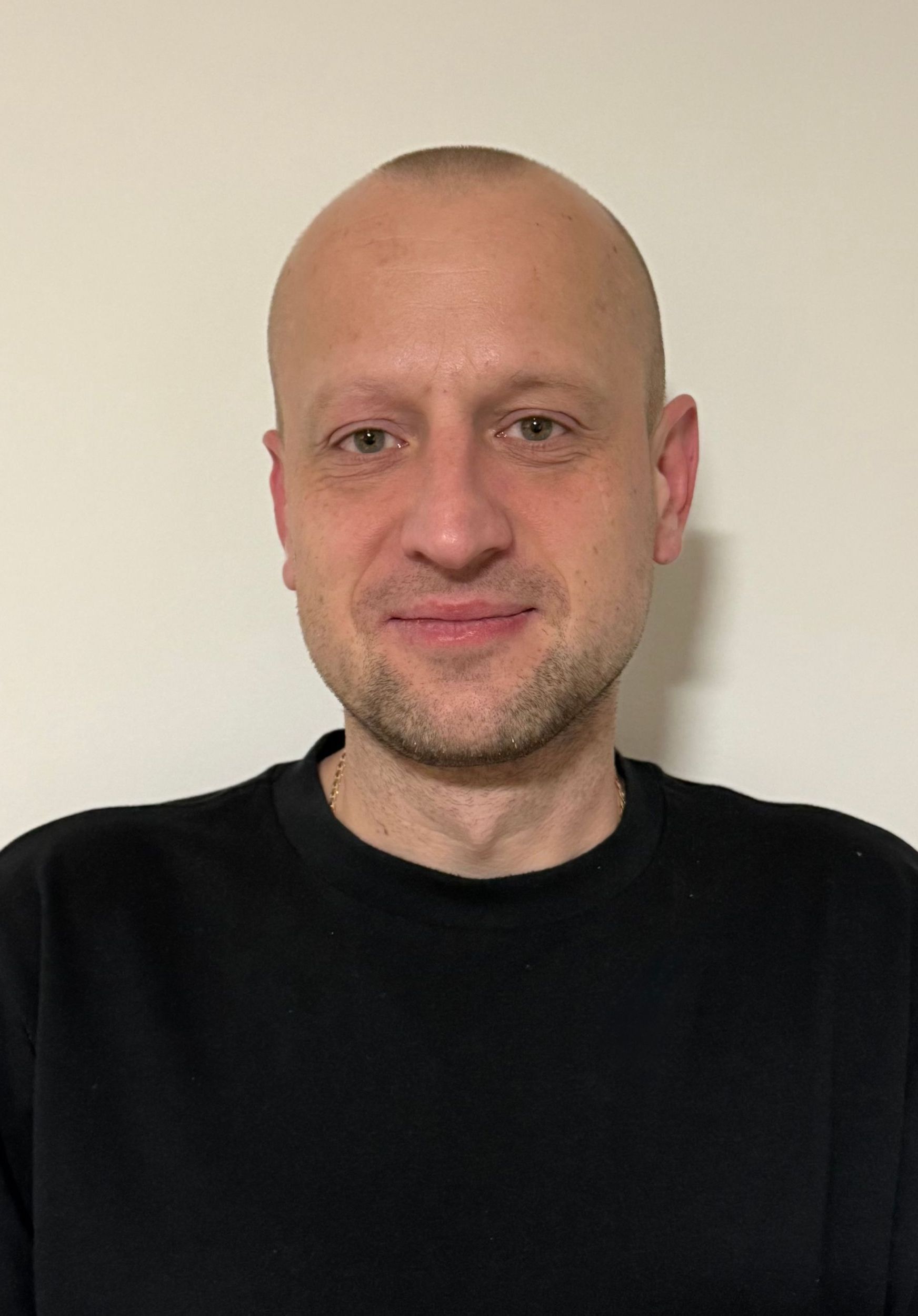 A bald person with light stubble wearing a black long-sleeve shirt against a plain, off-white background.