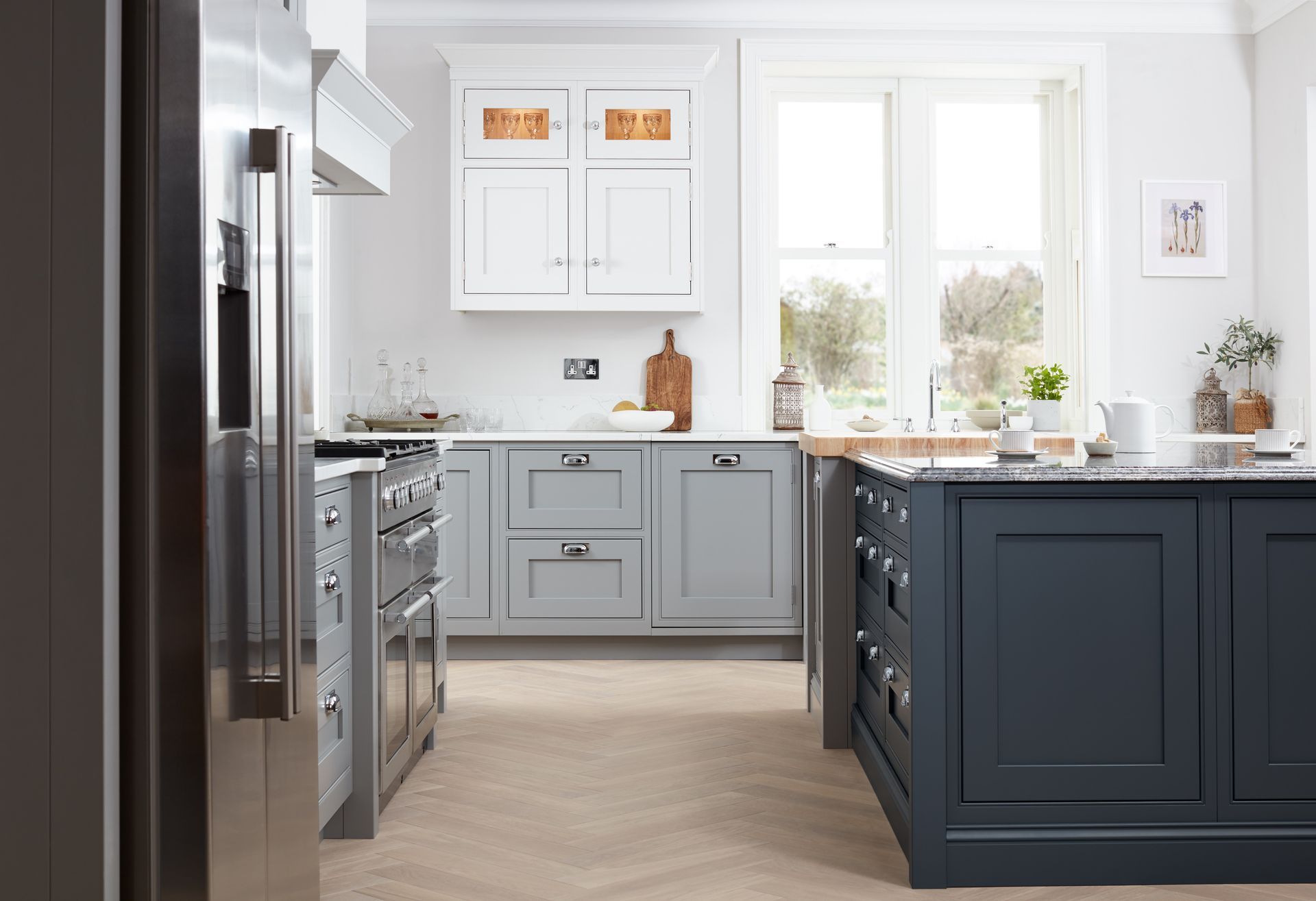 A modern kitchen featuring white upper cabinets, light gray lower cabinets, and a dark blue kitchen island with light floors.