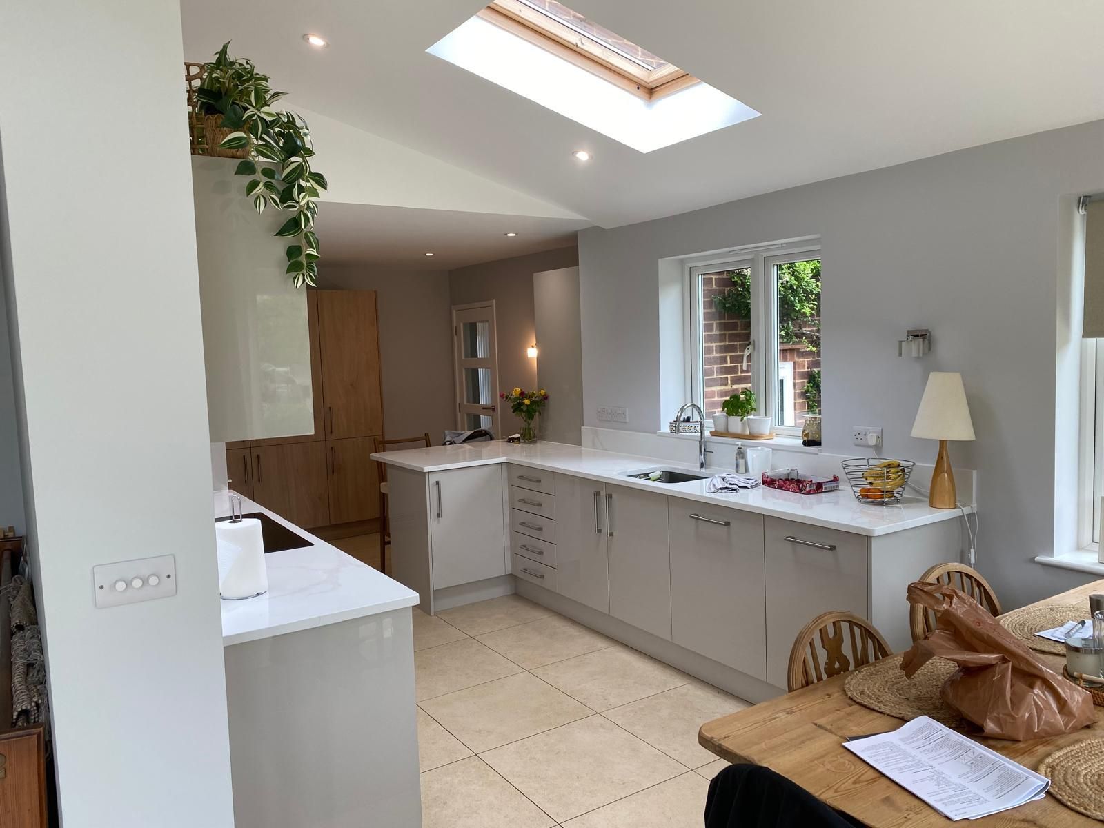 Modern, well-lit kitchen with light grey cabinetry, white countertops, a skylight, and a dining table in the foreground.
