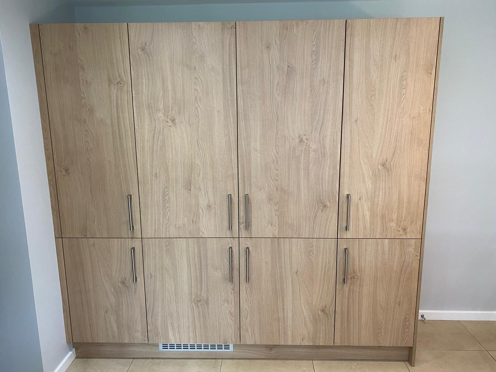 A tall, wood-grain storage cabinet with four upper and four lower cabinet doors, each featuring a vertical silver handle.