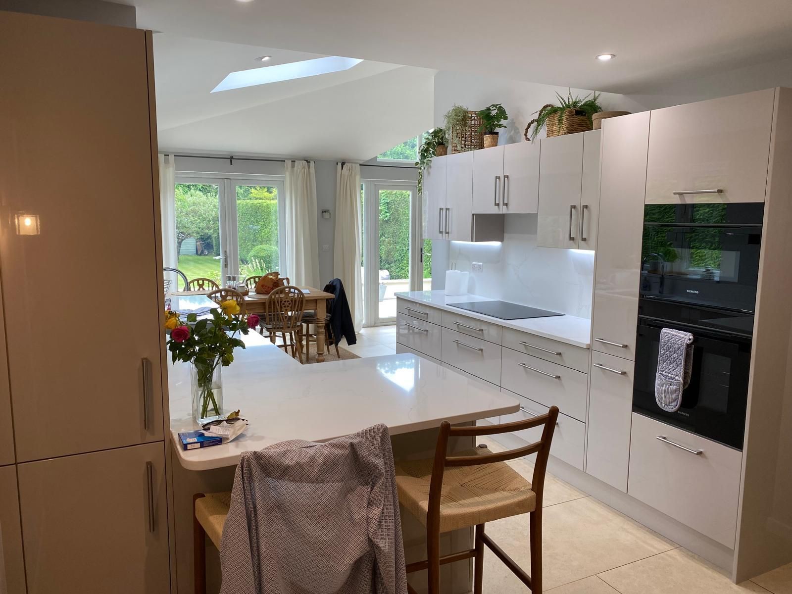 Modern kitchen with white cabinets, an island with two wooden chairs, and a bright dining area opening to a garden.