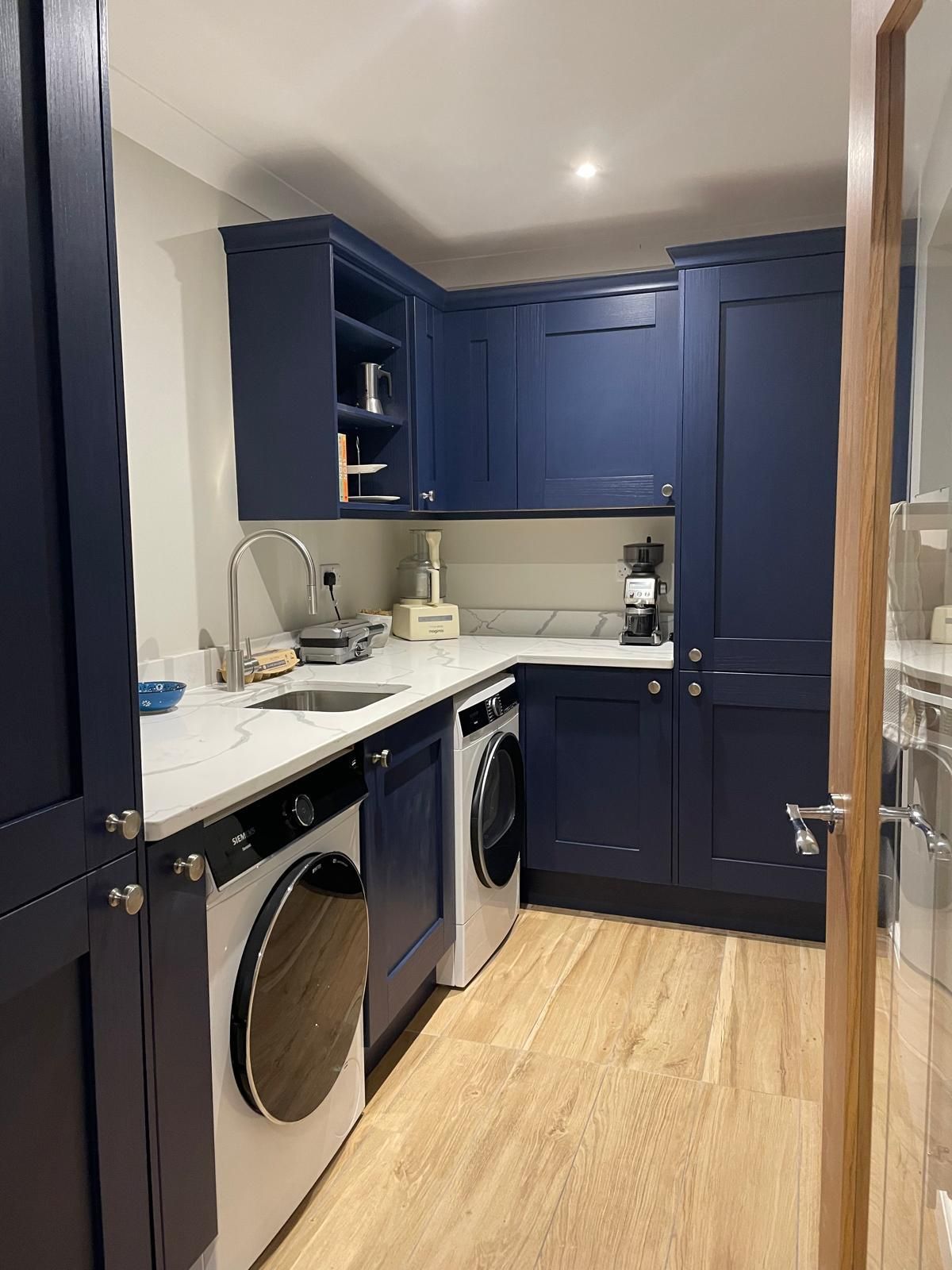 A laundry room featuring dark blue cabinets, white countertops, a stainless steel sink, and a built-in washing machine.