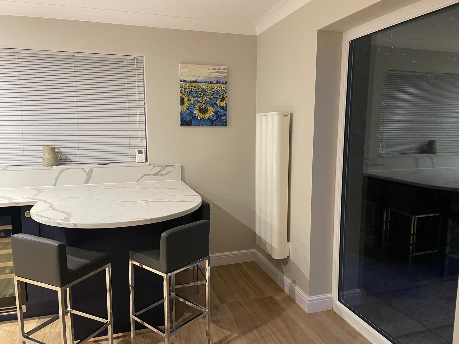A kitchen island with a marble countertop, two dark bar stools, a sunflower wall art, and a vertical white radiator.