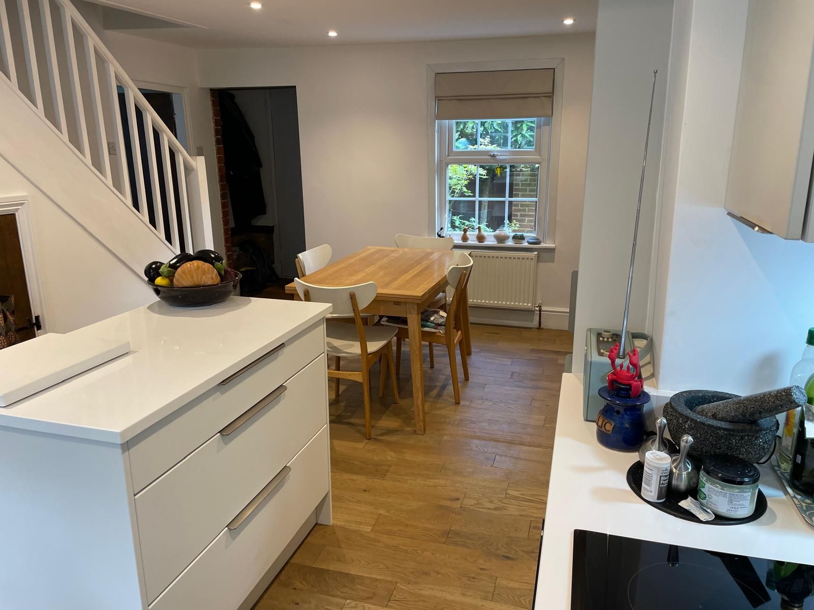 A bright, open-plan dining and kitchen area with white cabinets, a light wood dining table, and a staircase to the left.