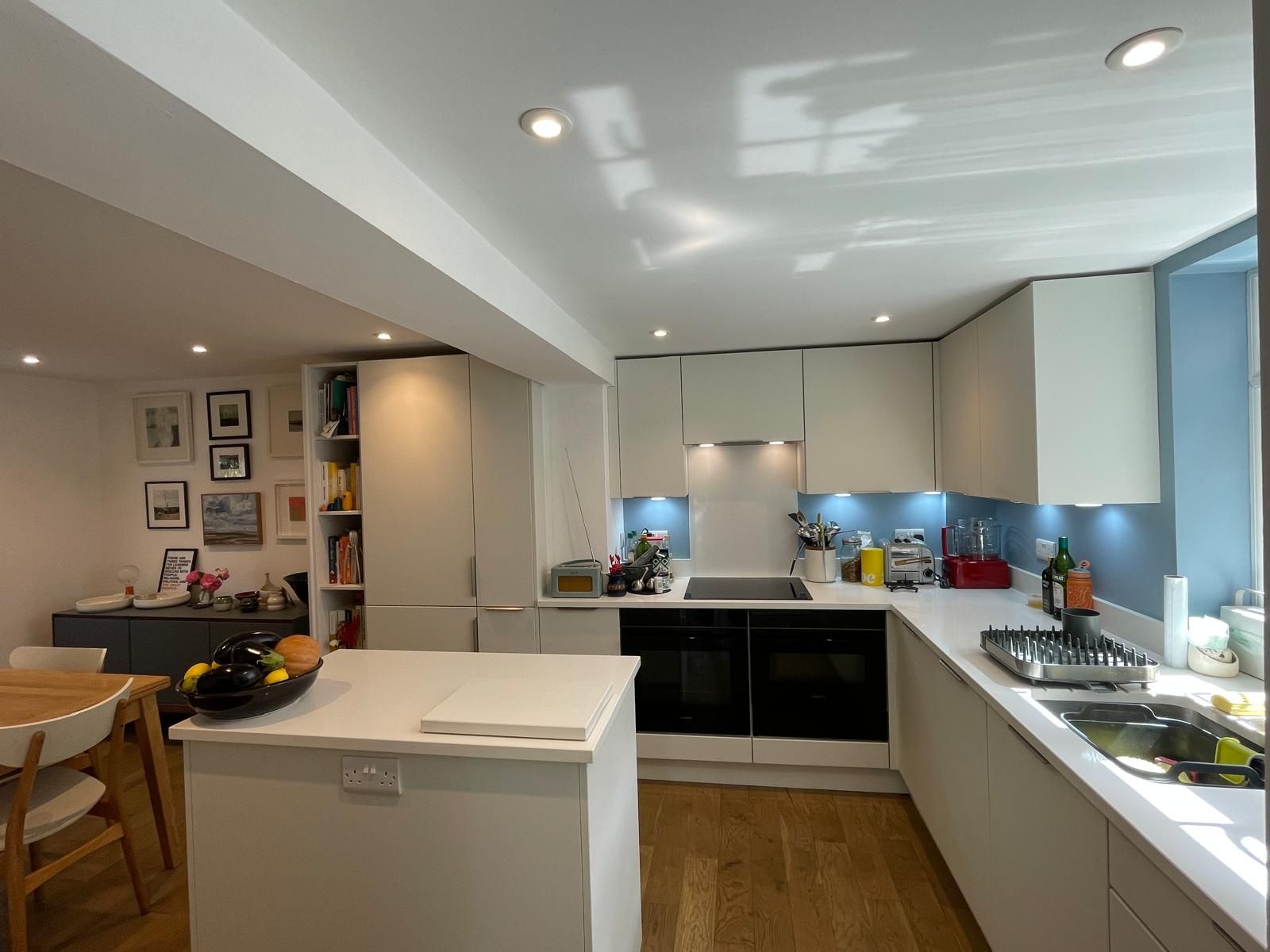 Modern kitchen with white cabinets, light wood flooring, a central island, and a blue backsplash behind the counters.