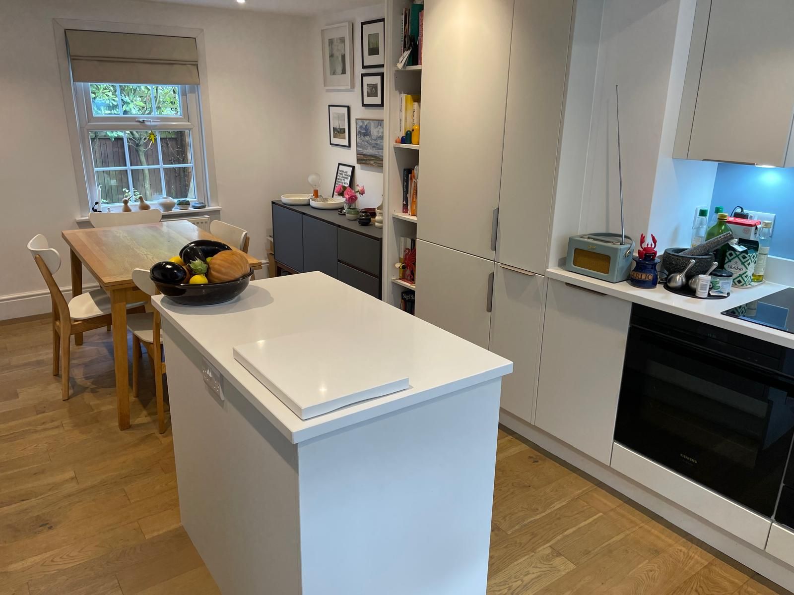 A modern, bright kitchen featuring a white center island, a wooden dining table, and sleek white cabinetry.