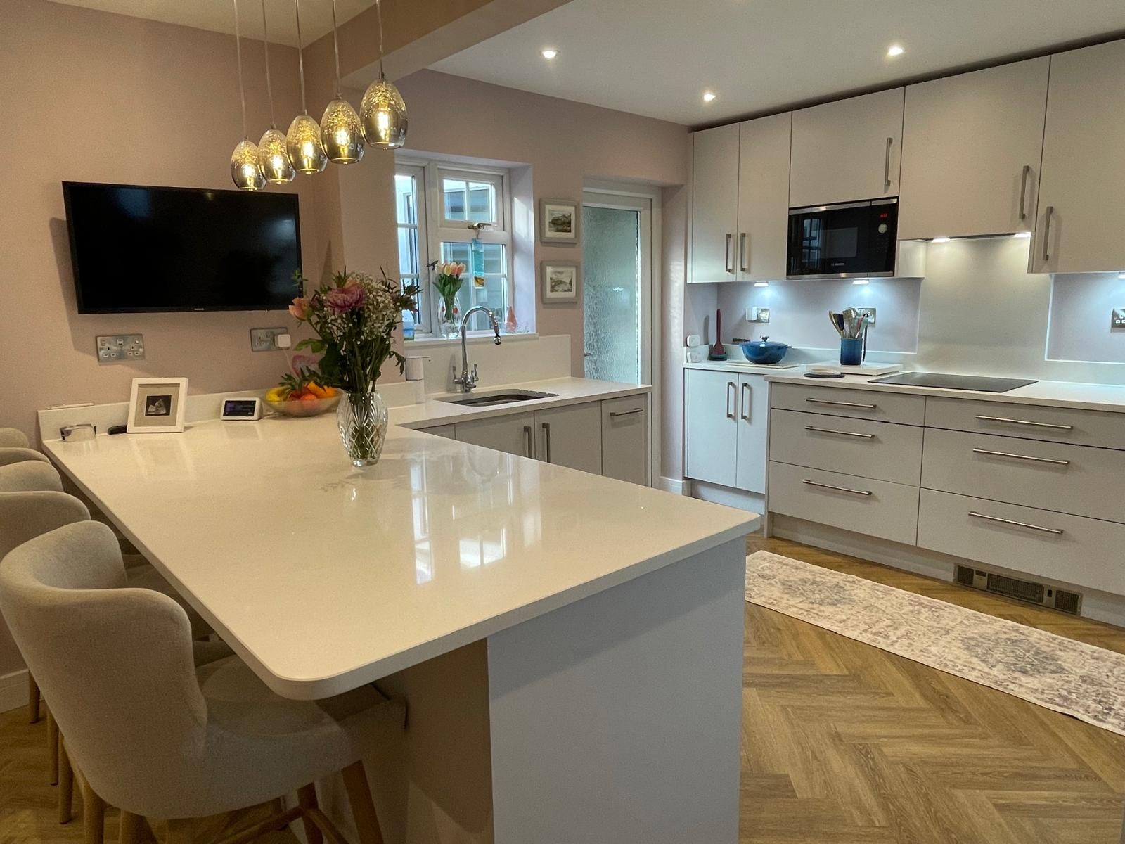 A modern, open-plan kitchen with pale cabinetry, white countertops, a central breakfast island, and wood flooring.