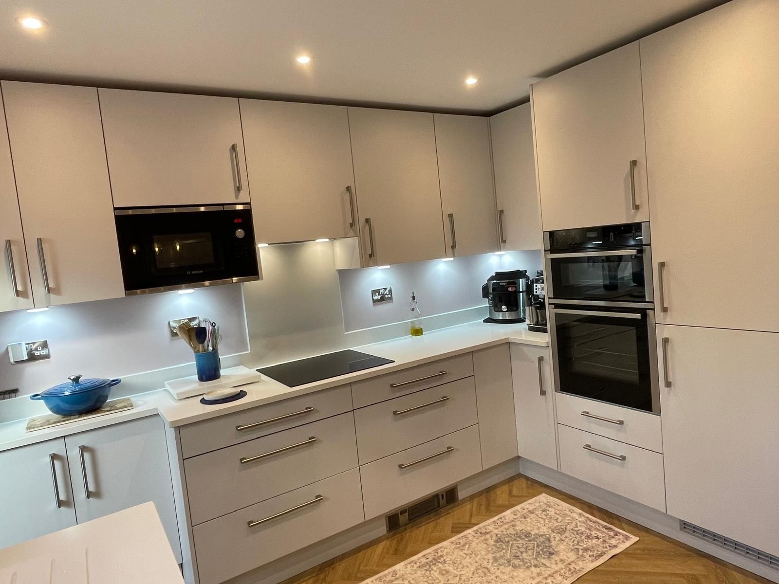 Modern U-shaped kitchen with light gray cabinets, integrated appliances, a white countertop, and herringbone wood flooring.