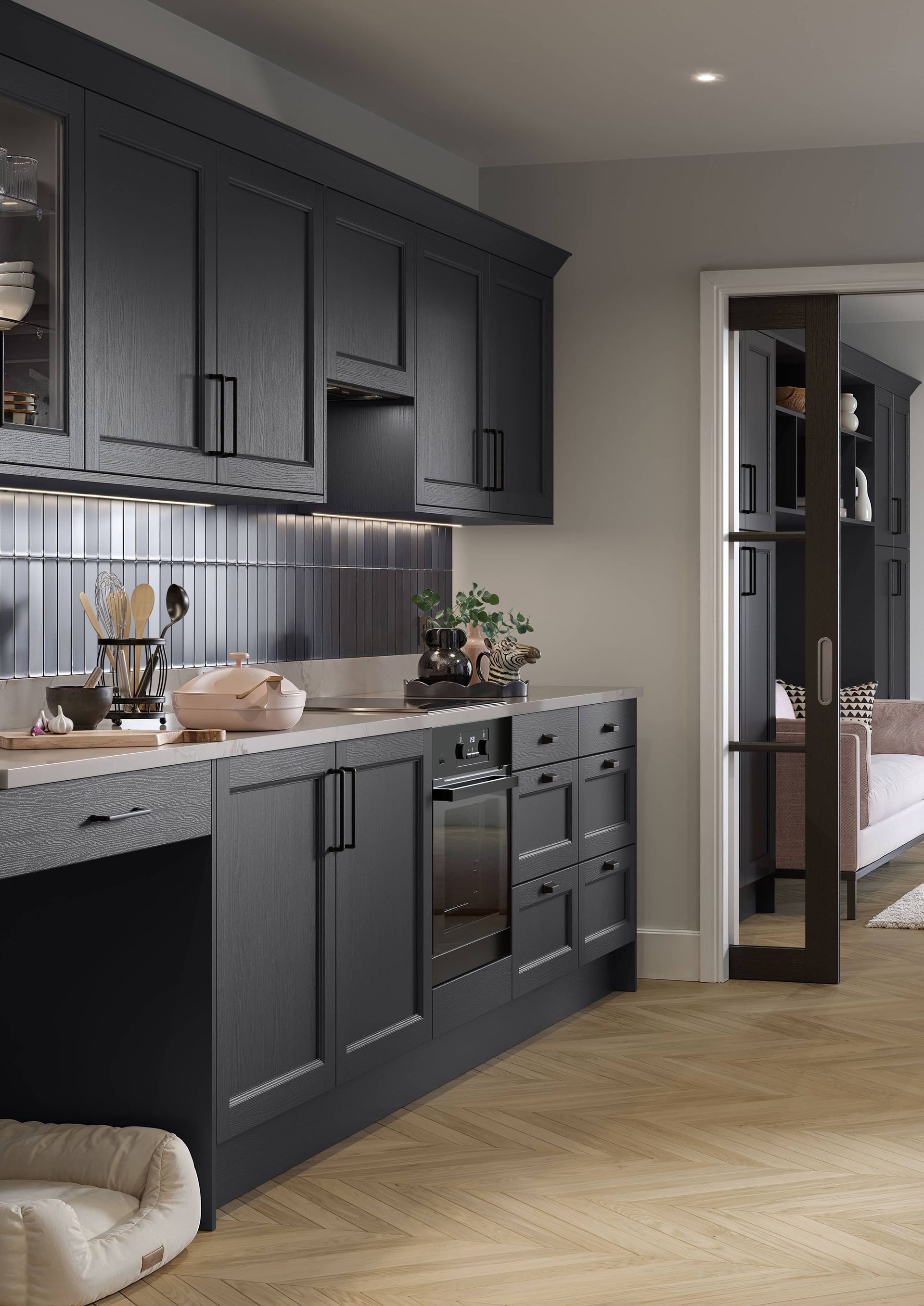 A dark-toned, modern kitchen with matte black cabinetry, a herringbone wooden floor, and an adjacent open doorway.