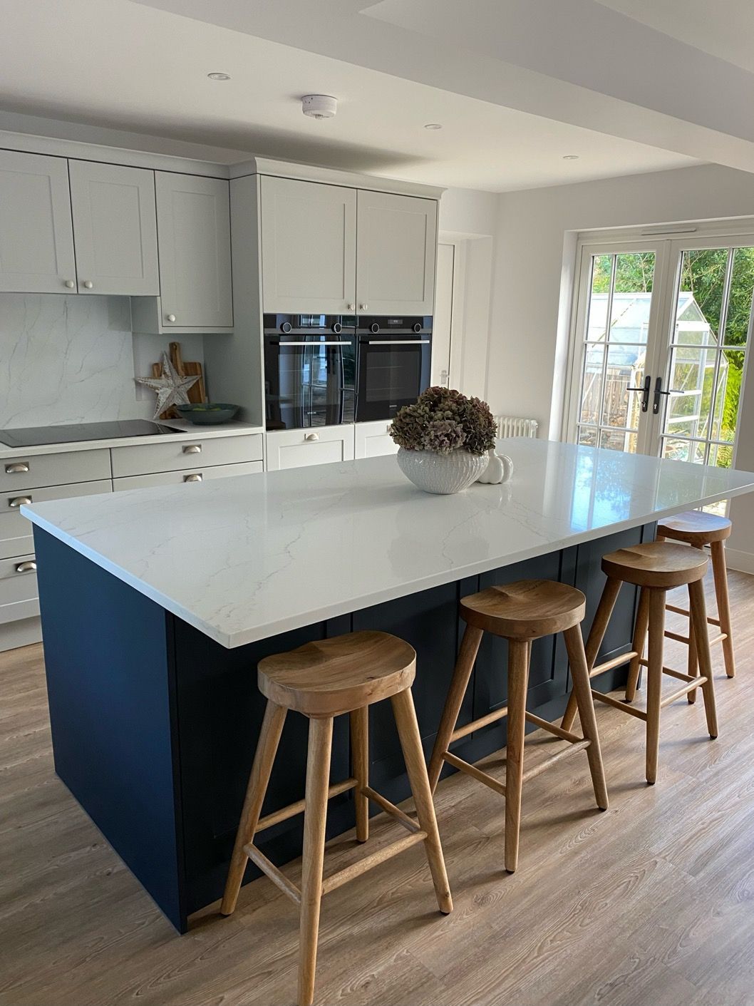 A bright kitchen featuring a white-topped island with three wooden bar stools in front of dark blue cabinetry.