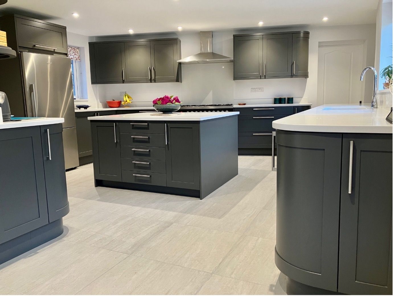 Modern kitchen with dark grey cabinets, white countertops, a central island, and stainless steel appliances.