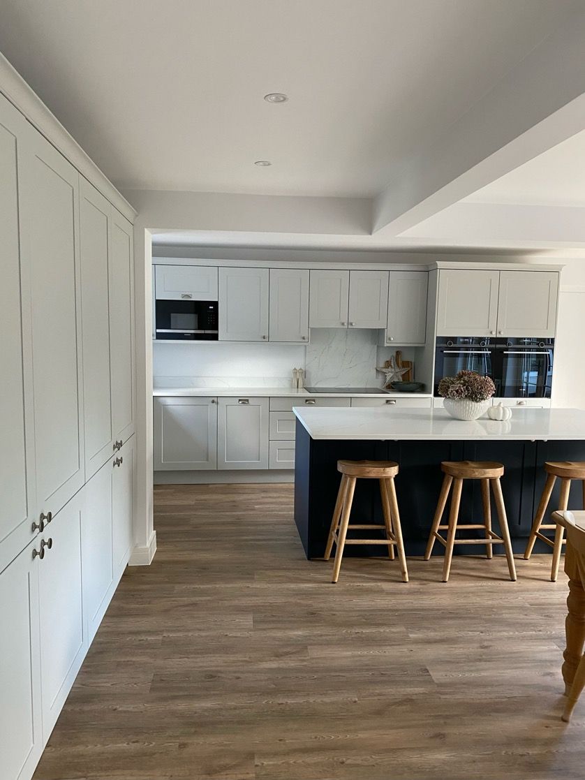A bright modern kitchen with white cabinets, a large dark blue kitchen island, and light wood flooring.