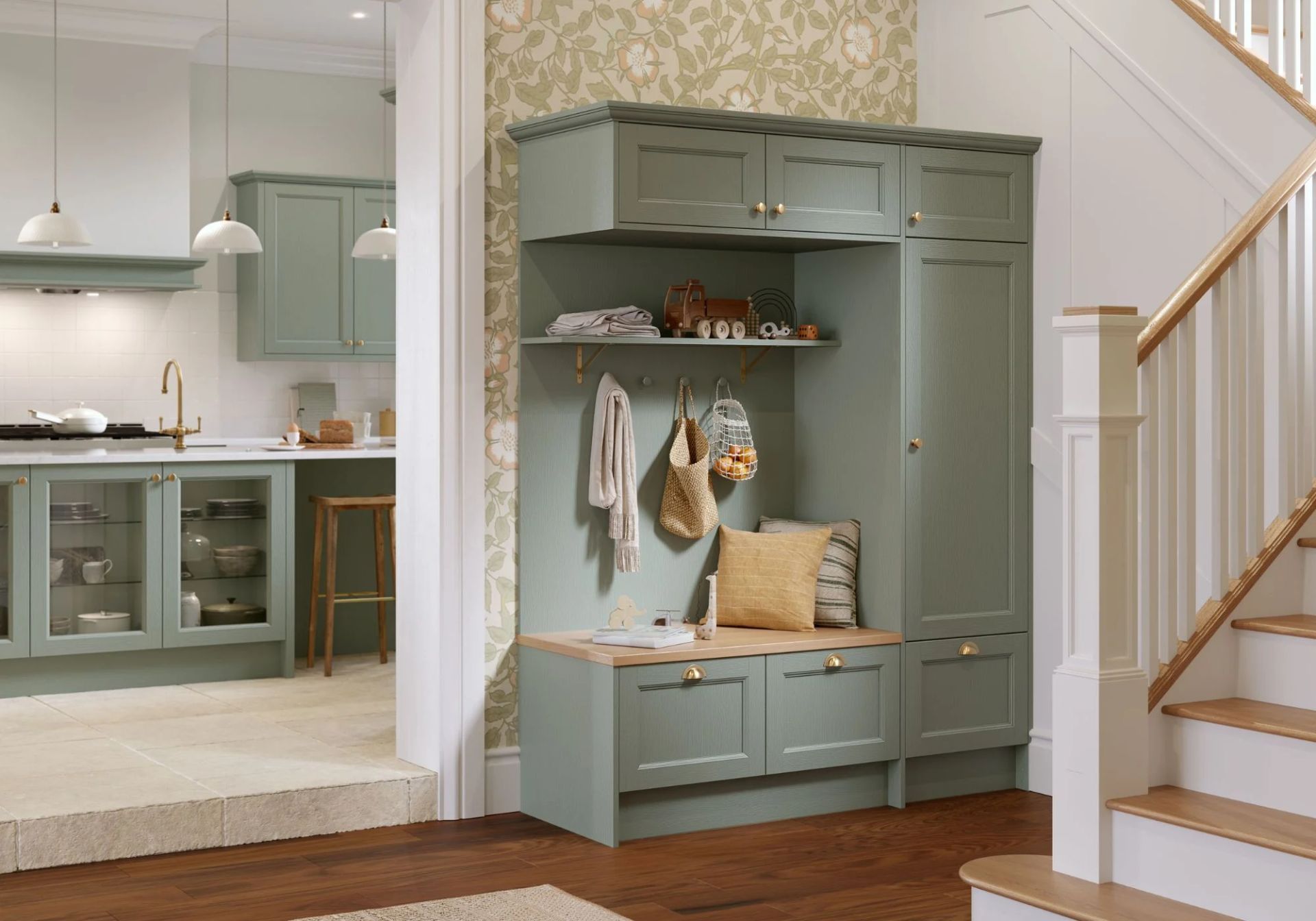 A sage green mudroom built-in cabinet with seating, hooks, and shelving, positioned near a kitchen doorway and stairs.