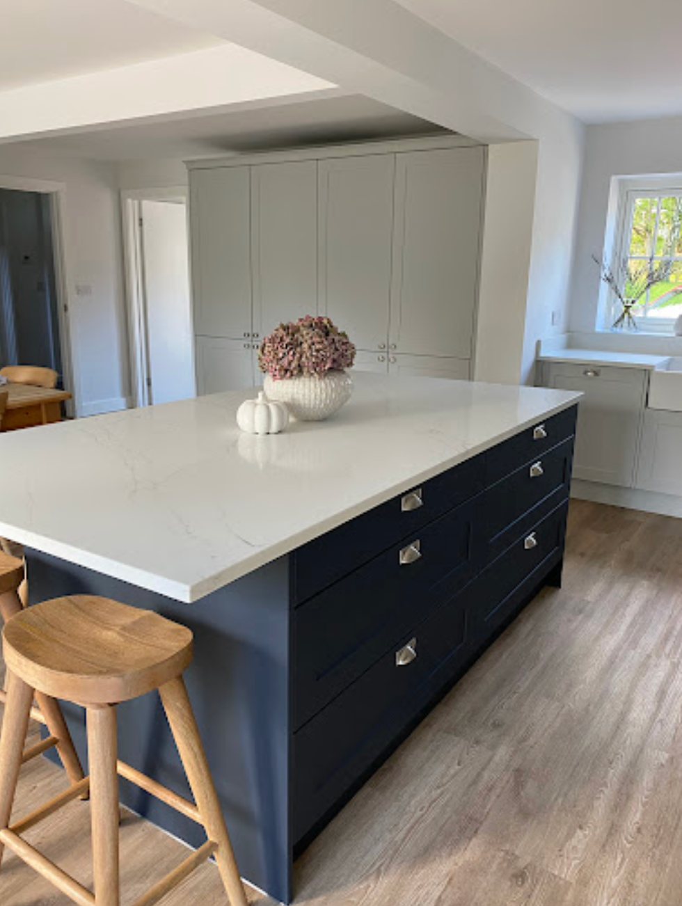A navy kitchen island with a white marble-style countertop and wooden stools, centered in a modern kitchen.
