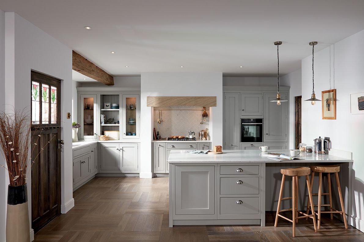 A spacious, modern farmhouse kitchen with light gray cabinetry, a wooden ceiling beam, white island, and wooden stools.