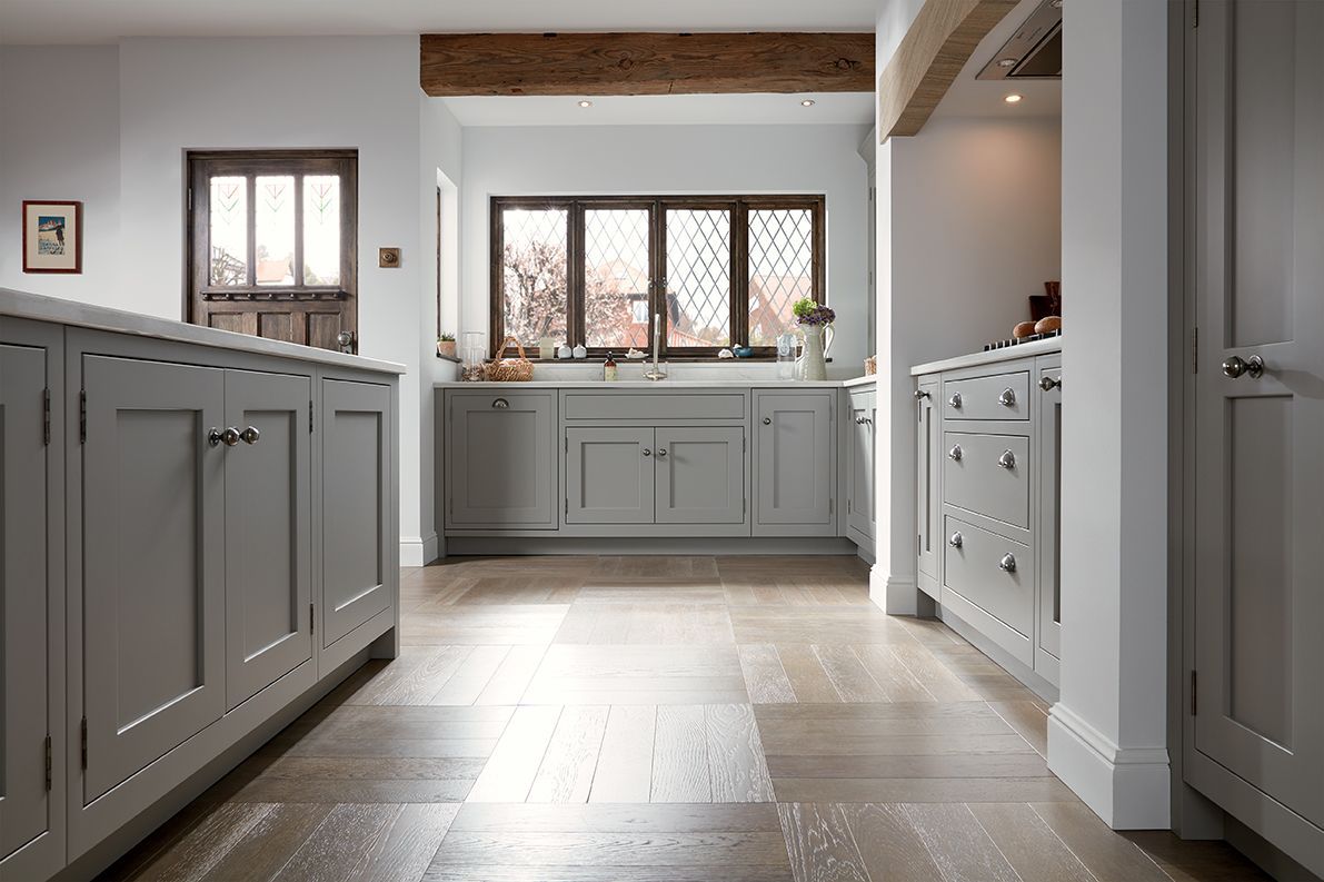 A bright, modern kitchen featuring gray shaker-style cabinets, hardwood floors, and a large wooden ceiling beam.