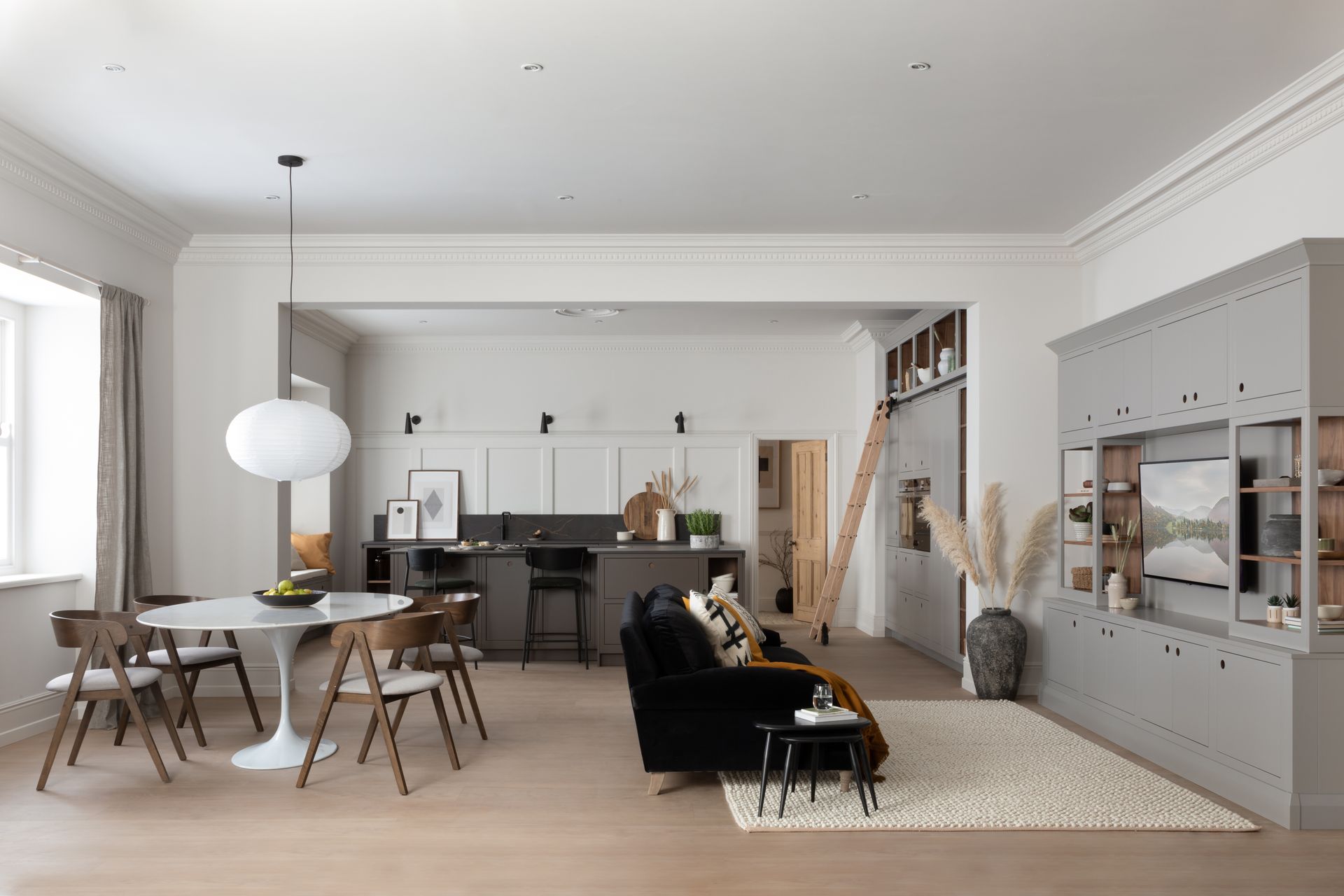 A modern open-concept living area with a dining table, black sofa, kitchen island, and built-in grey cabinetry.