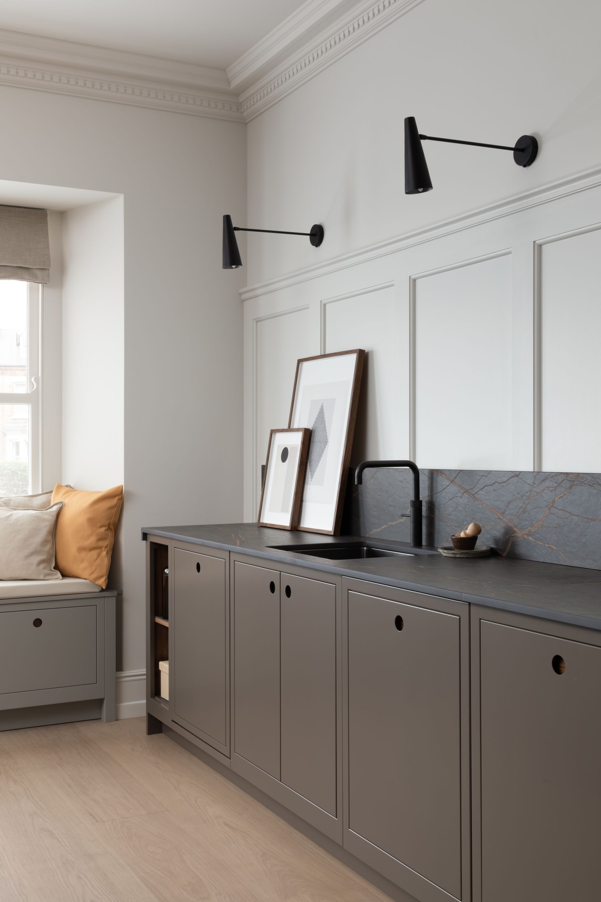 A modern kitchen featuring matte grey cabinets, a dark stone countertop, white paneled walls, and two black wall lamps.