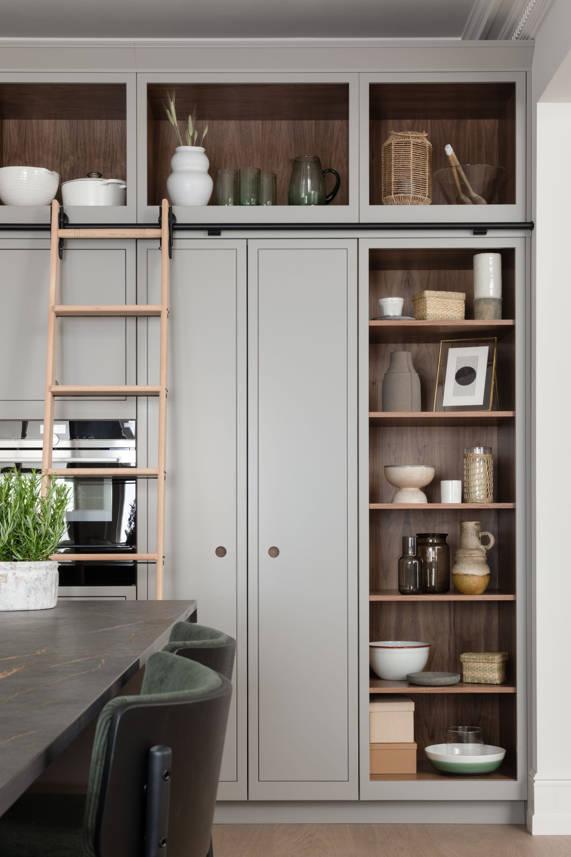 Modern kitchen featuring light gray cabinetry, a wooden rolling ladder, and built-in shelving with decorative decor.