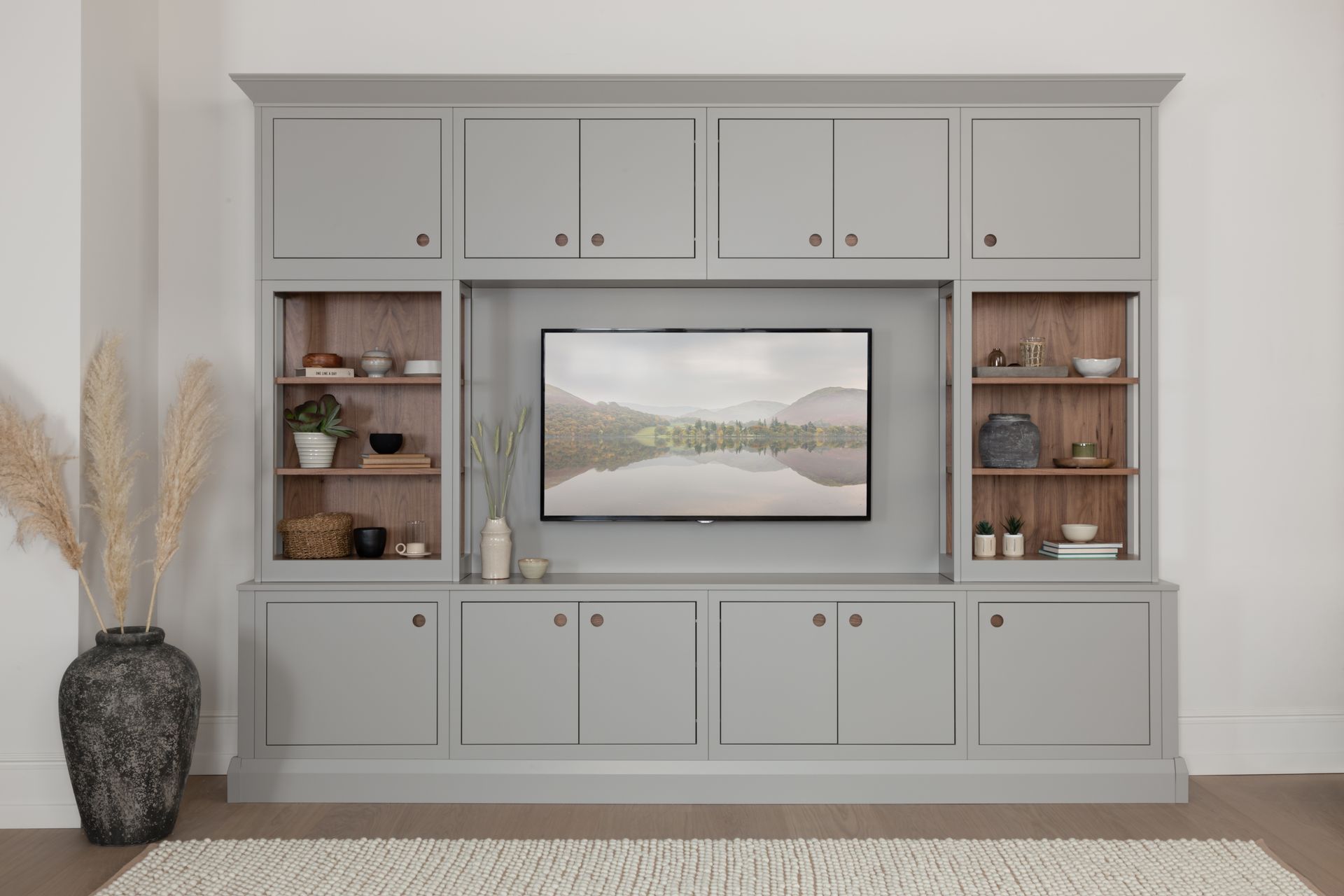 A large gray built-in media wall unit featuring upper cabinets, open wooden shelving, a central TV, and lower cupboards.