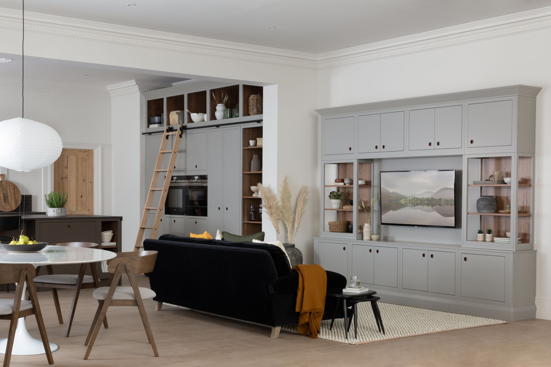 A bright open-plan living room with light gray cabinetry, a black sofa, a rolling ladder, and a round white dining table.