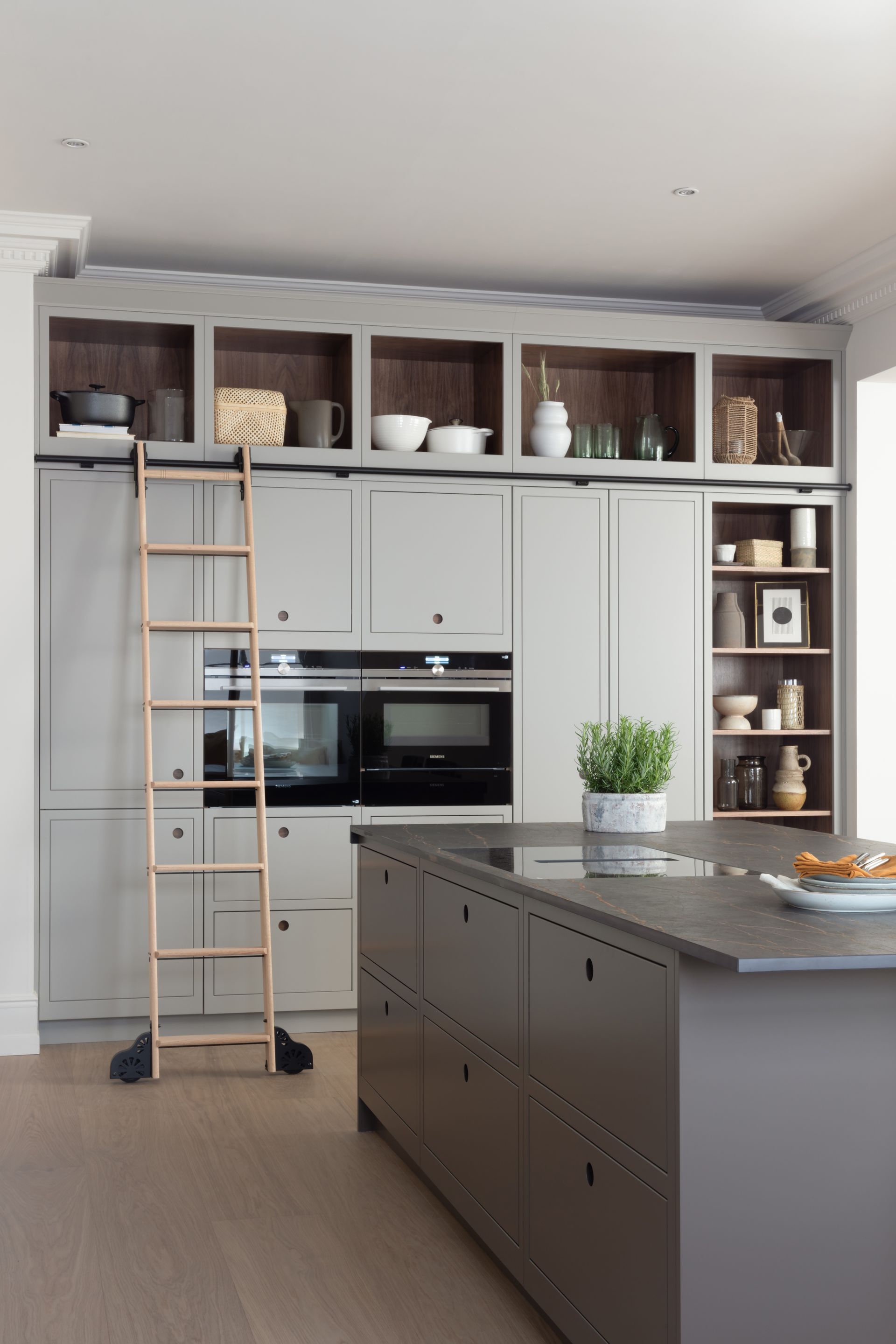 Modern kitchen with a gray island, matching cabinetry, open top shelving, and a rolling wooden library ladder.