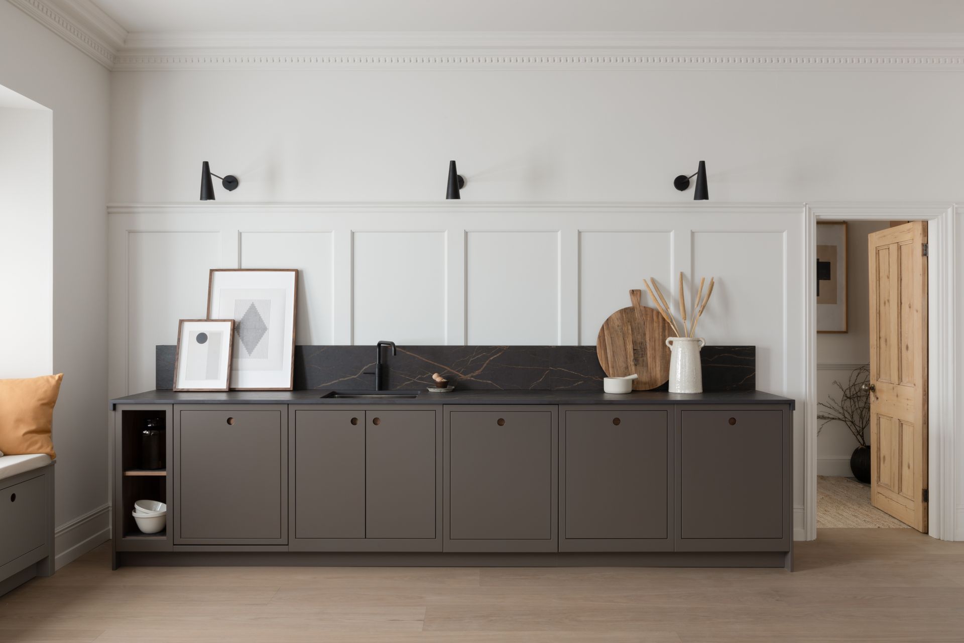 A kitchen console with dark gray cabinets and a black marble backsplash against a white paneled wall with three sconces.