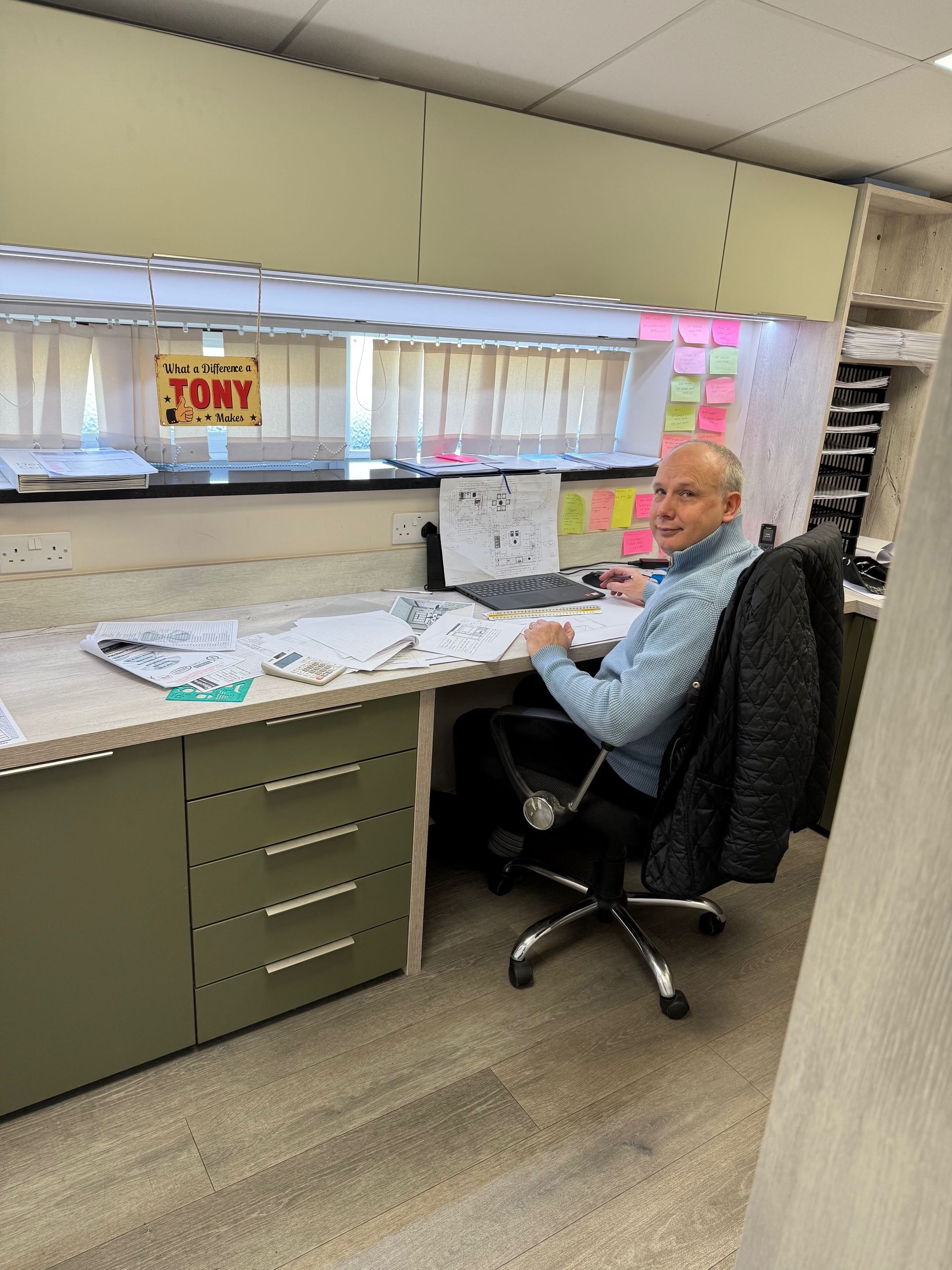 A person wearing a blue sweater sits at a light green office desk, working on documents in a well-lit workspace.
