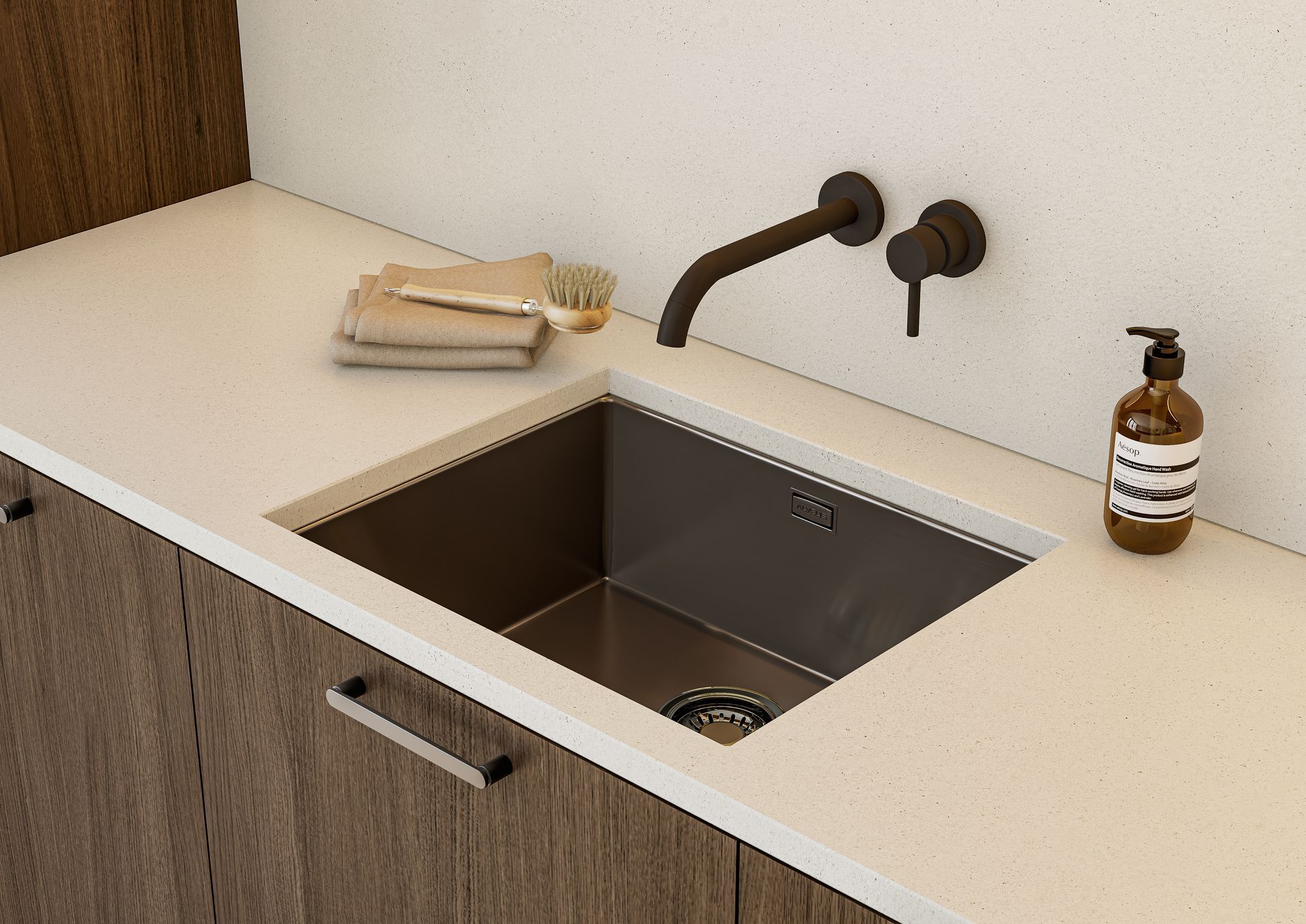 A stainless steel sink with a dark bronze wall-mounted faucet and soap dispenser set into a light-colored countertop.