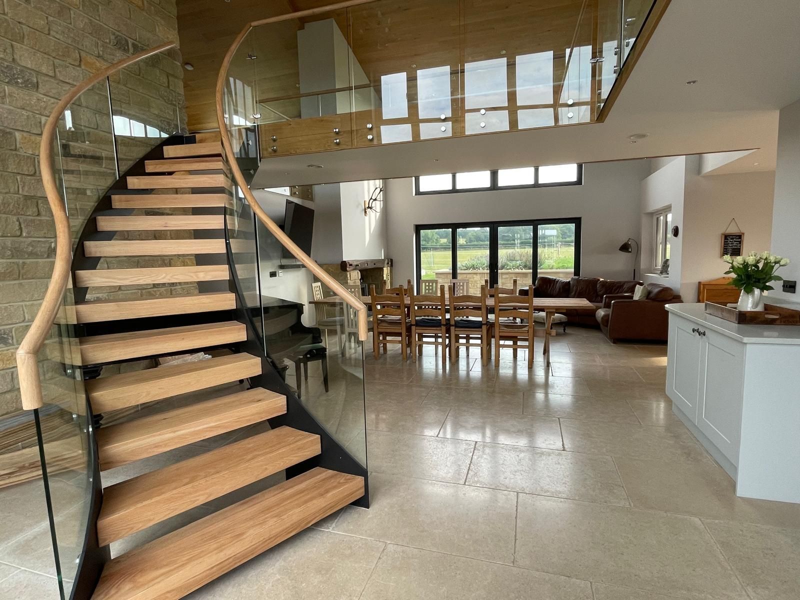 A modern open-plan home featuring a curved wood and glass staircase leading to a mezzanine, overlooking a dining area.